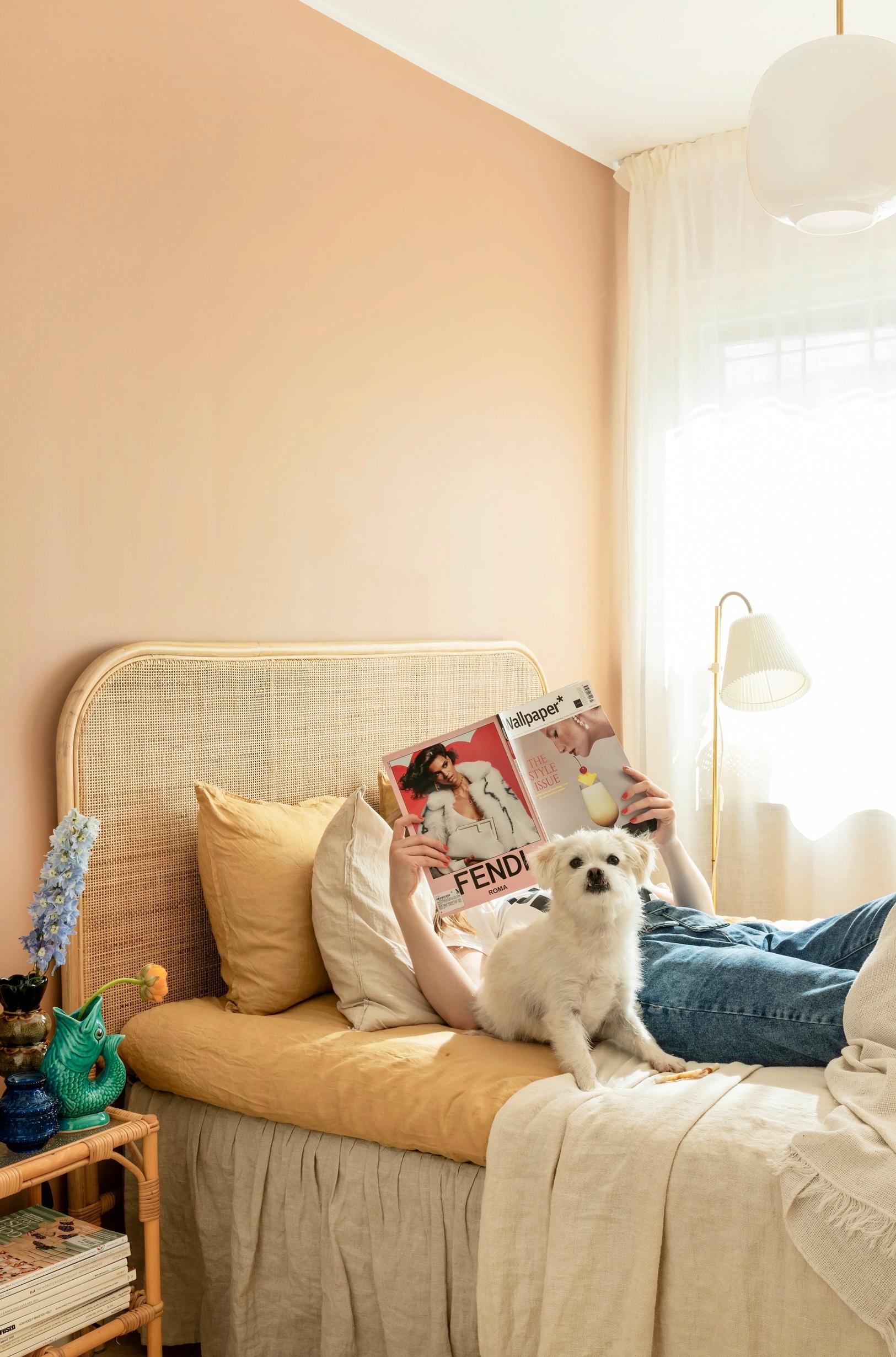 Anna-Maria relaxing and reading a magazine in the rattan-headboard bed with her dog.