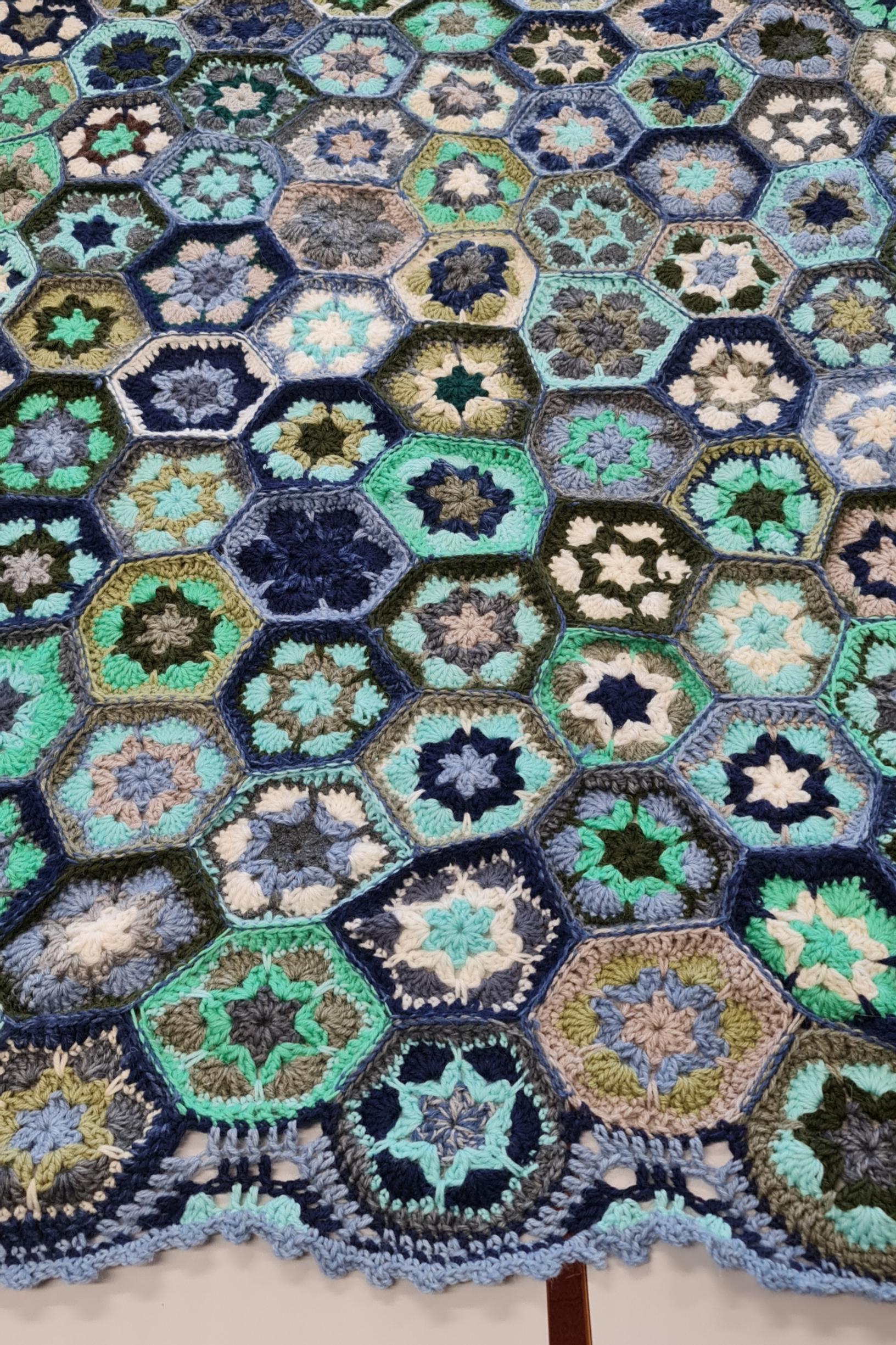 A close-up of a blue and green crocheted blanket featuring African flower motifs