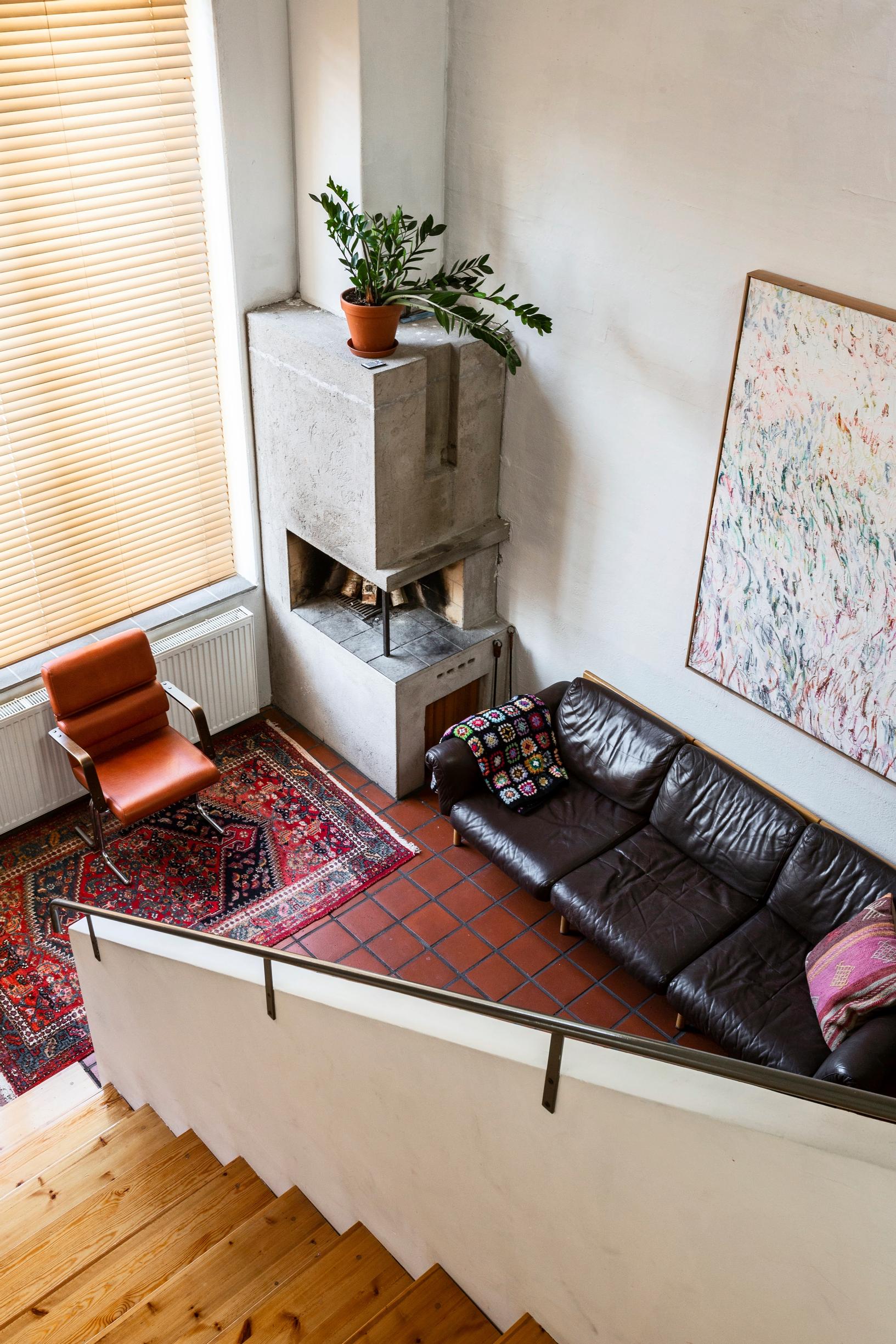 Home in Alvar Aalto’s former heating plant, view from upstairs down to the lounge area with a leather sofa, armchair, and open fireplace