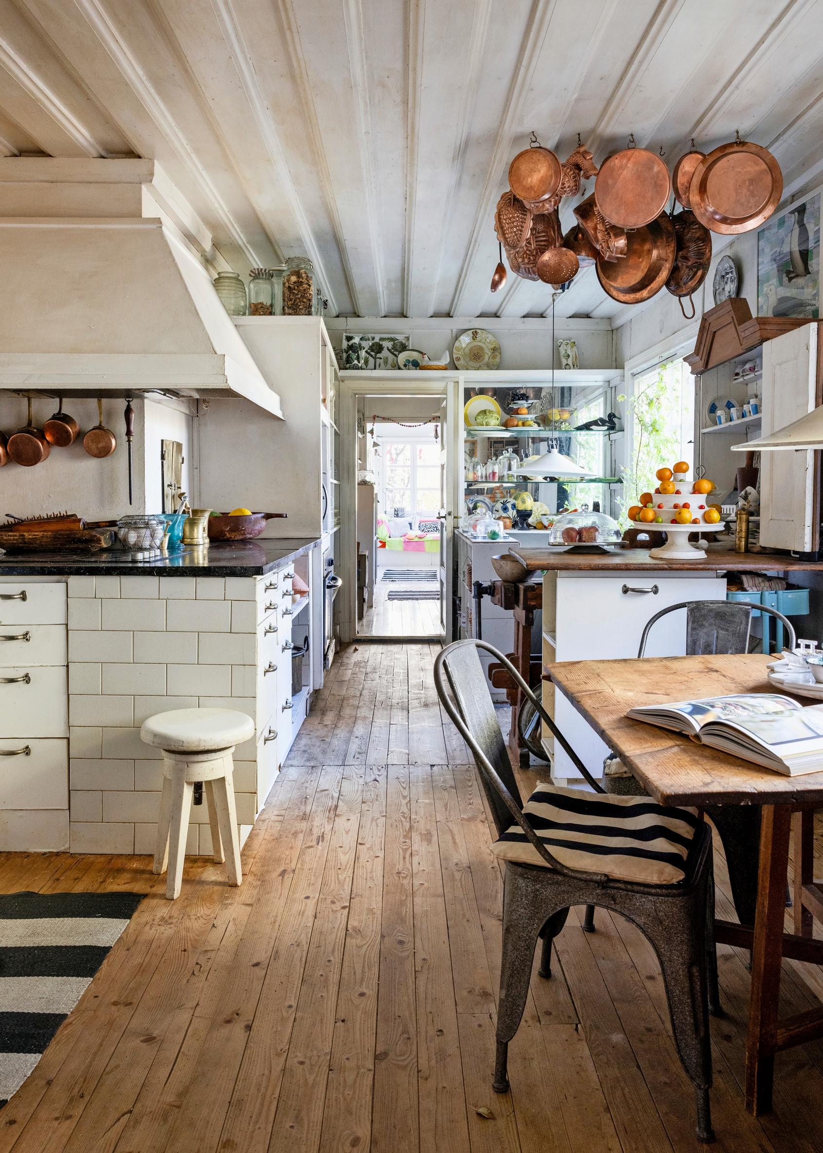 Kitchen with a large white-painted range hood, a table, and copper pots hanging from the ceiling.