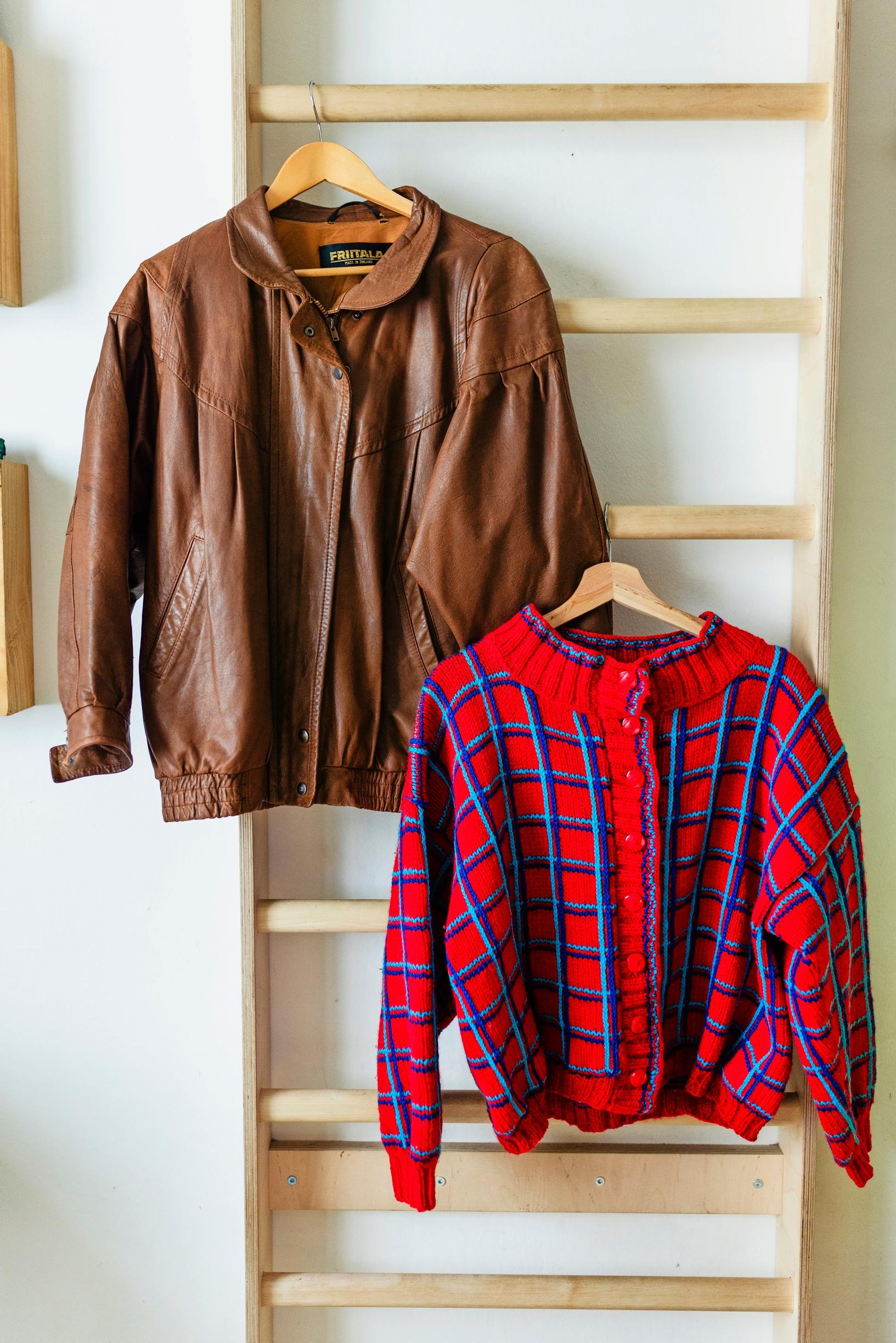 A brown leather jacket and a red-toned wool cardigan on hangers.