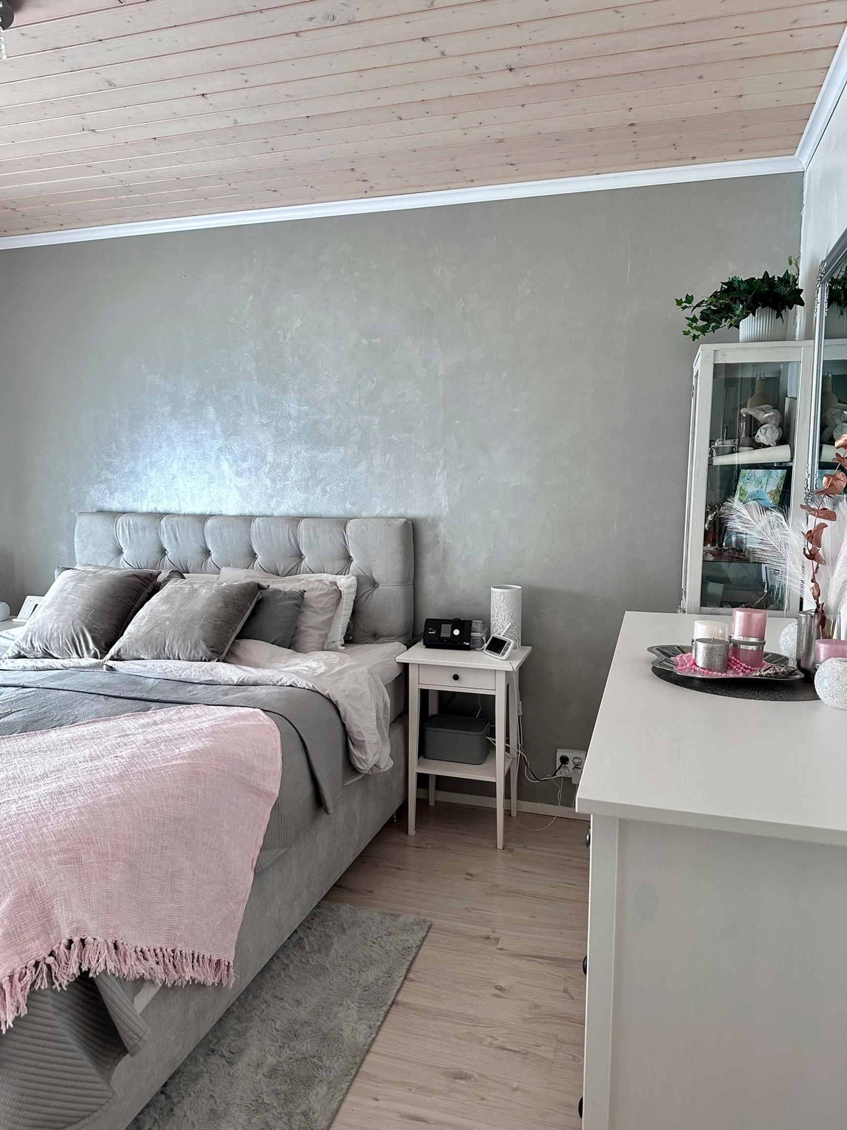 A double bed with a padded headboard matching the wall stands against it. The bed frame and coverlet share the same gray tones.