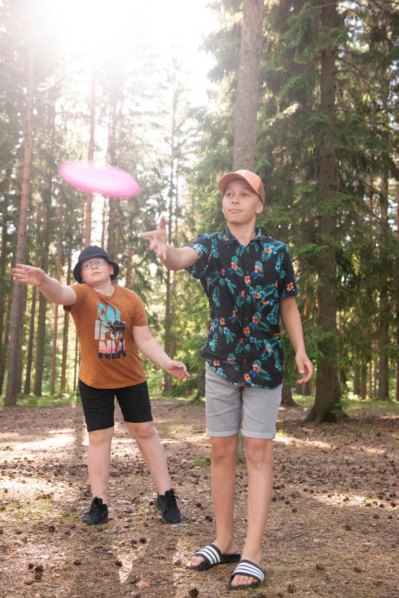 two boys tossing a frisbee with a pine forest in the background
