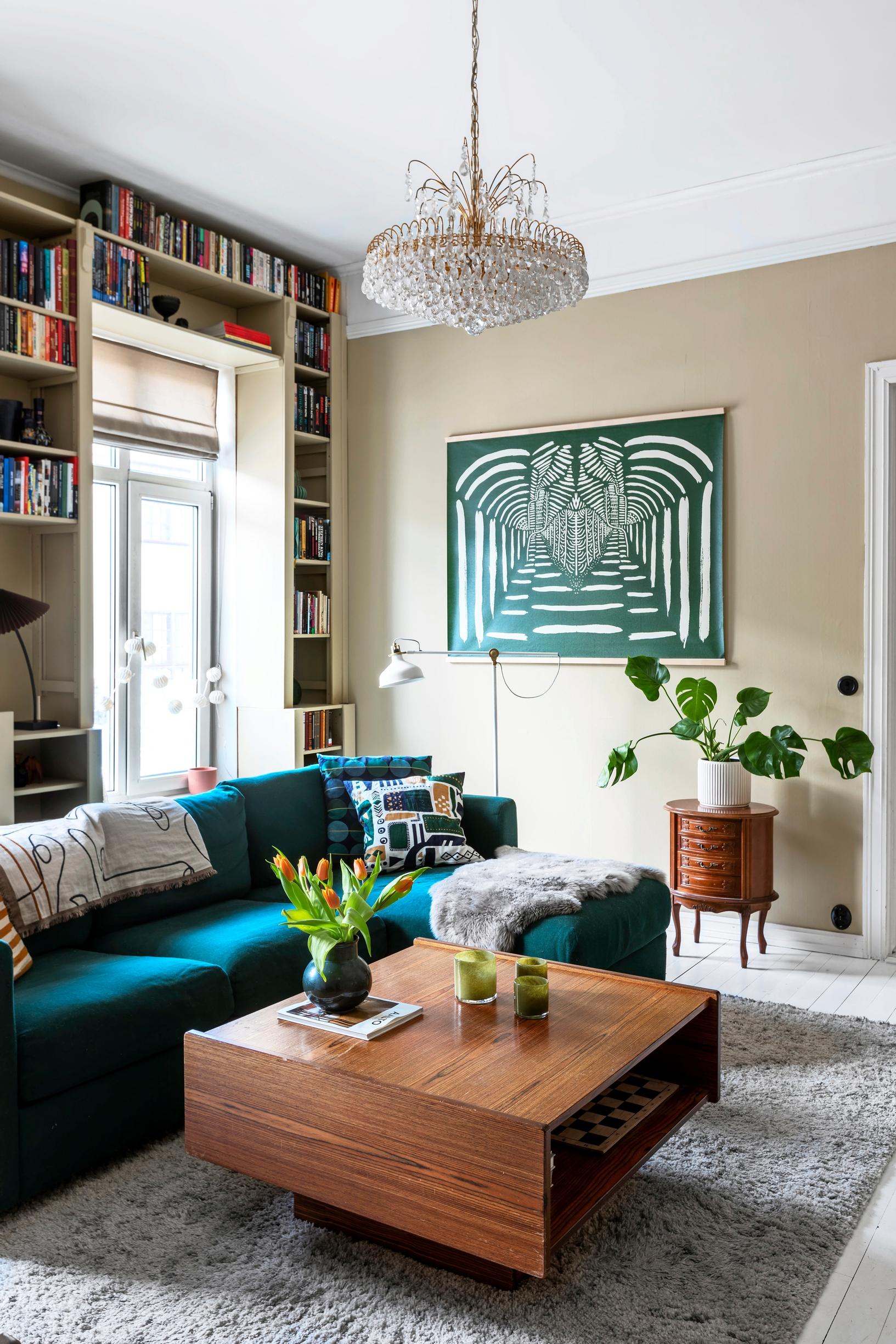 A living room with a bookcase, a crystal chandelier, and a work of art.