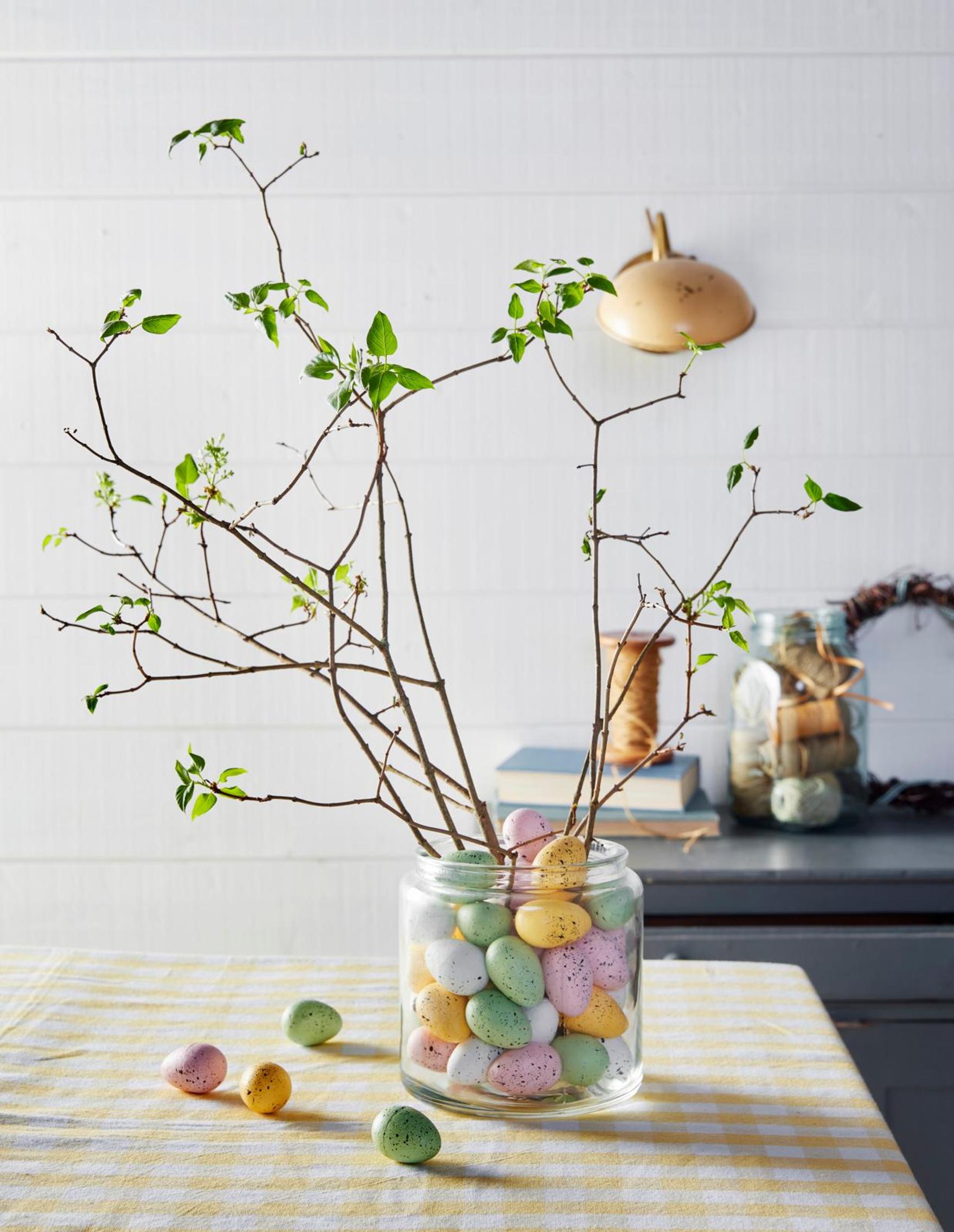 Spring branches arranged in a glass vase filled with decorative eggs.