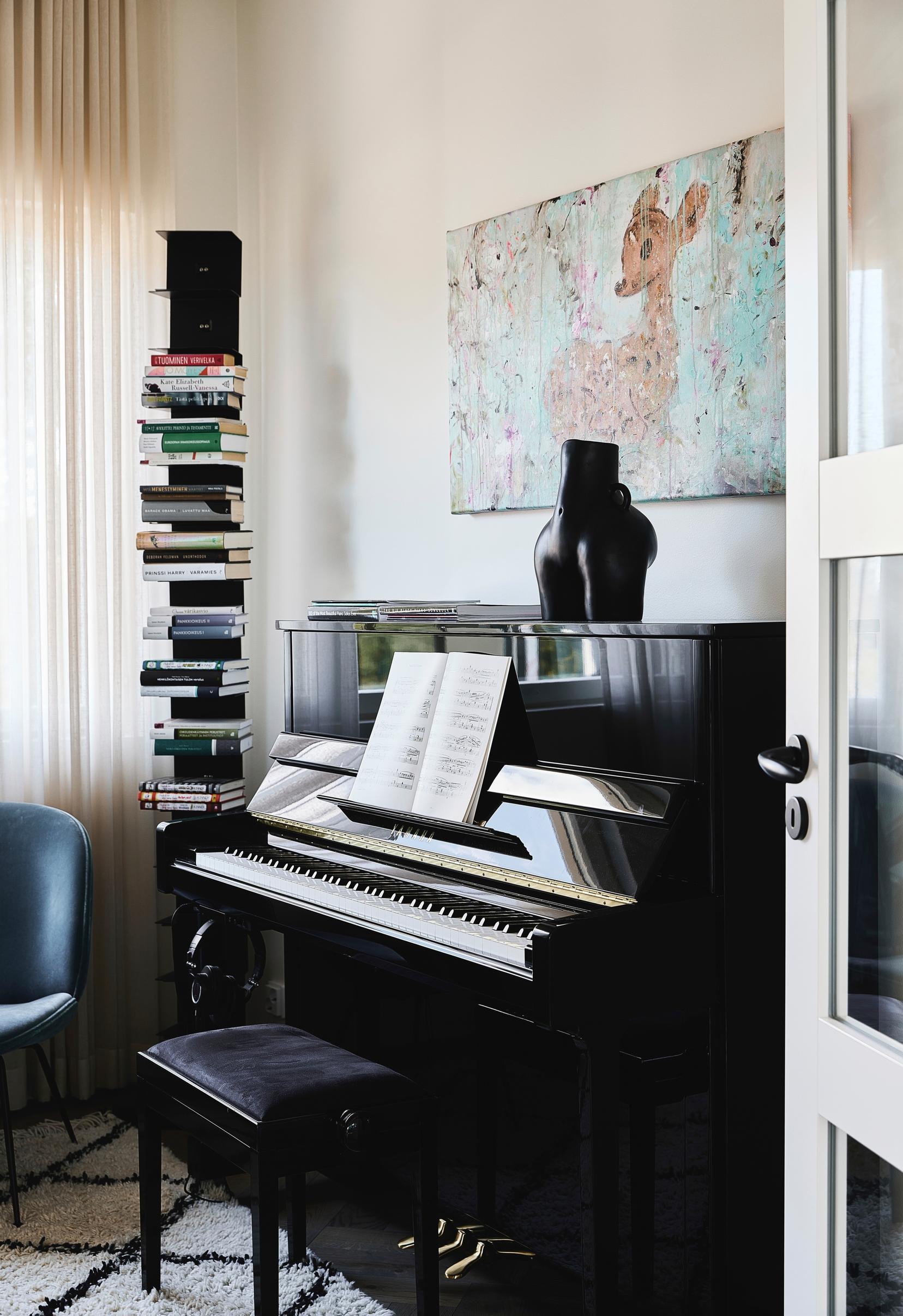 A piano room with a black piano, a book stand in the corner, and a bamboo-themed painting on the wall.