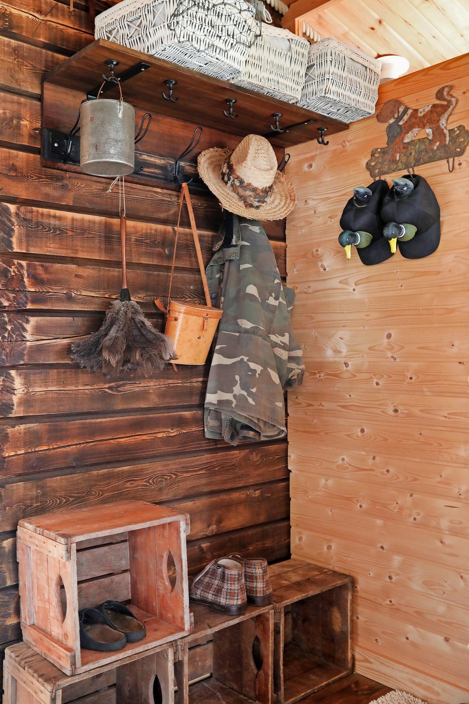 Binoculars, a jacket, and a hat hanging on the log wall, with wooden crates in the foreground.