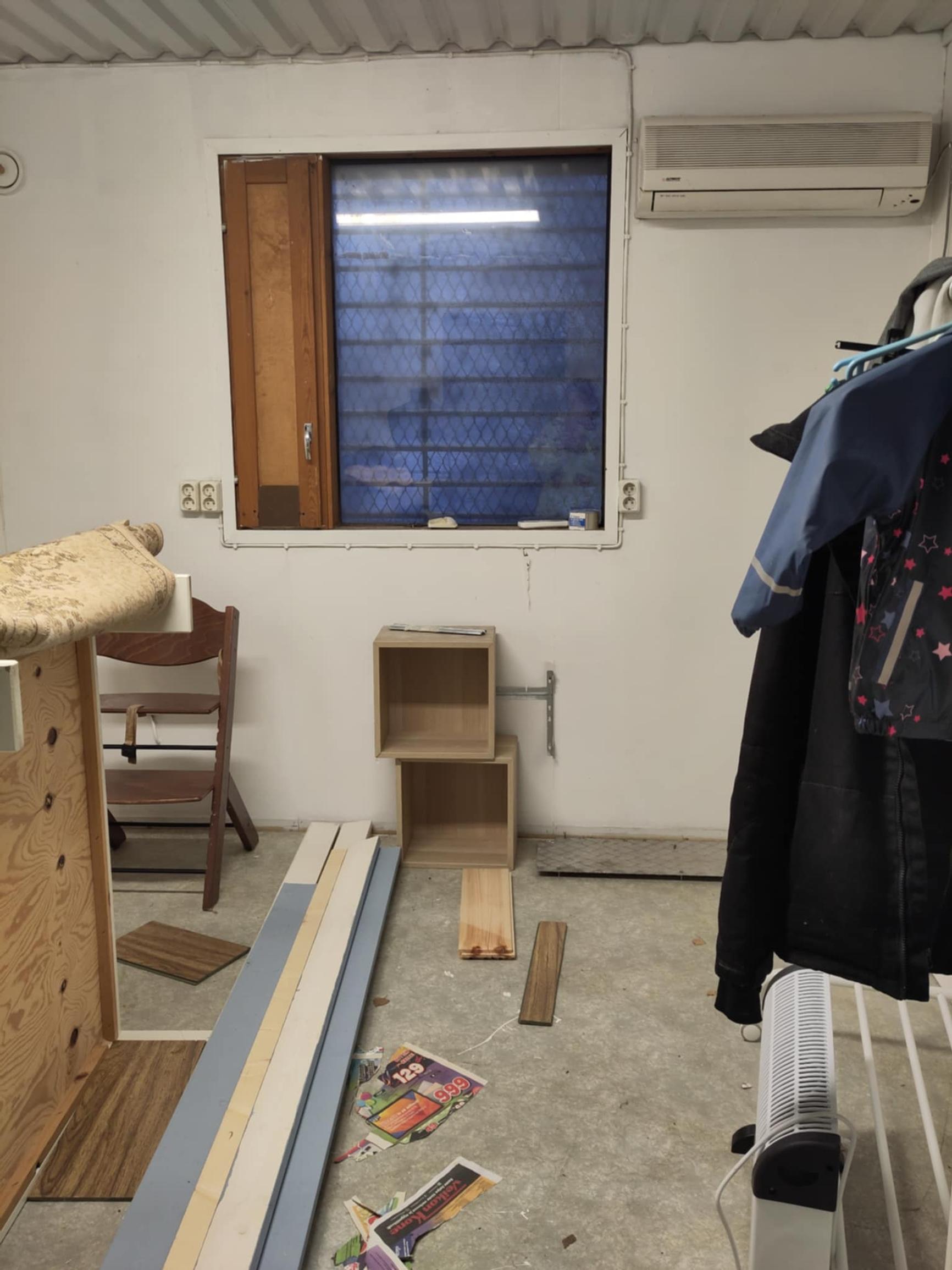Interior of an office container with some clothes and a chair, and a window in the back wall.