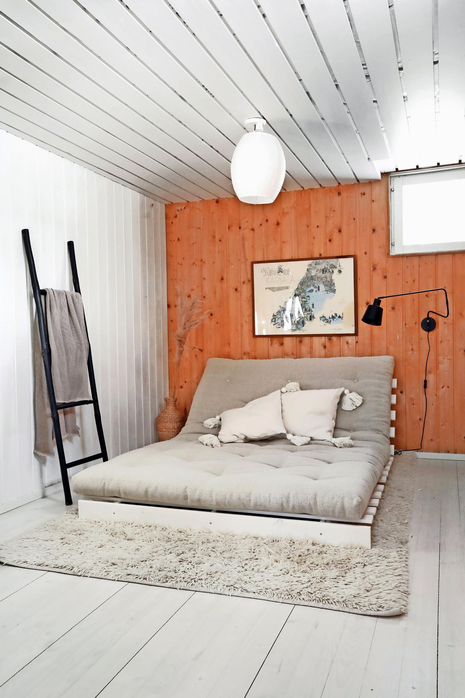 A wood-toned paneled end wall, with a white-painted wall on the right. In the center, a low futon bed.