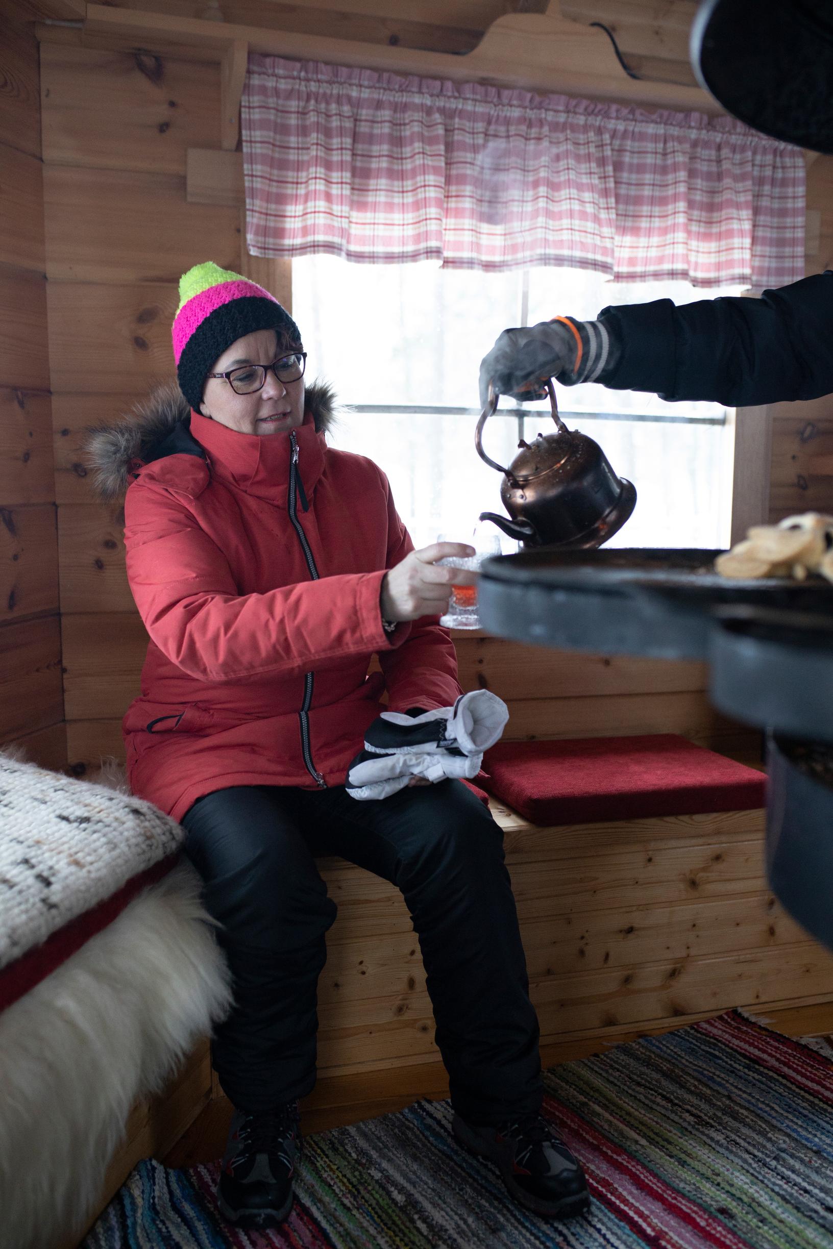 Coffee made in a pot being poured for a seated woman inside a wintery gazebo.