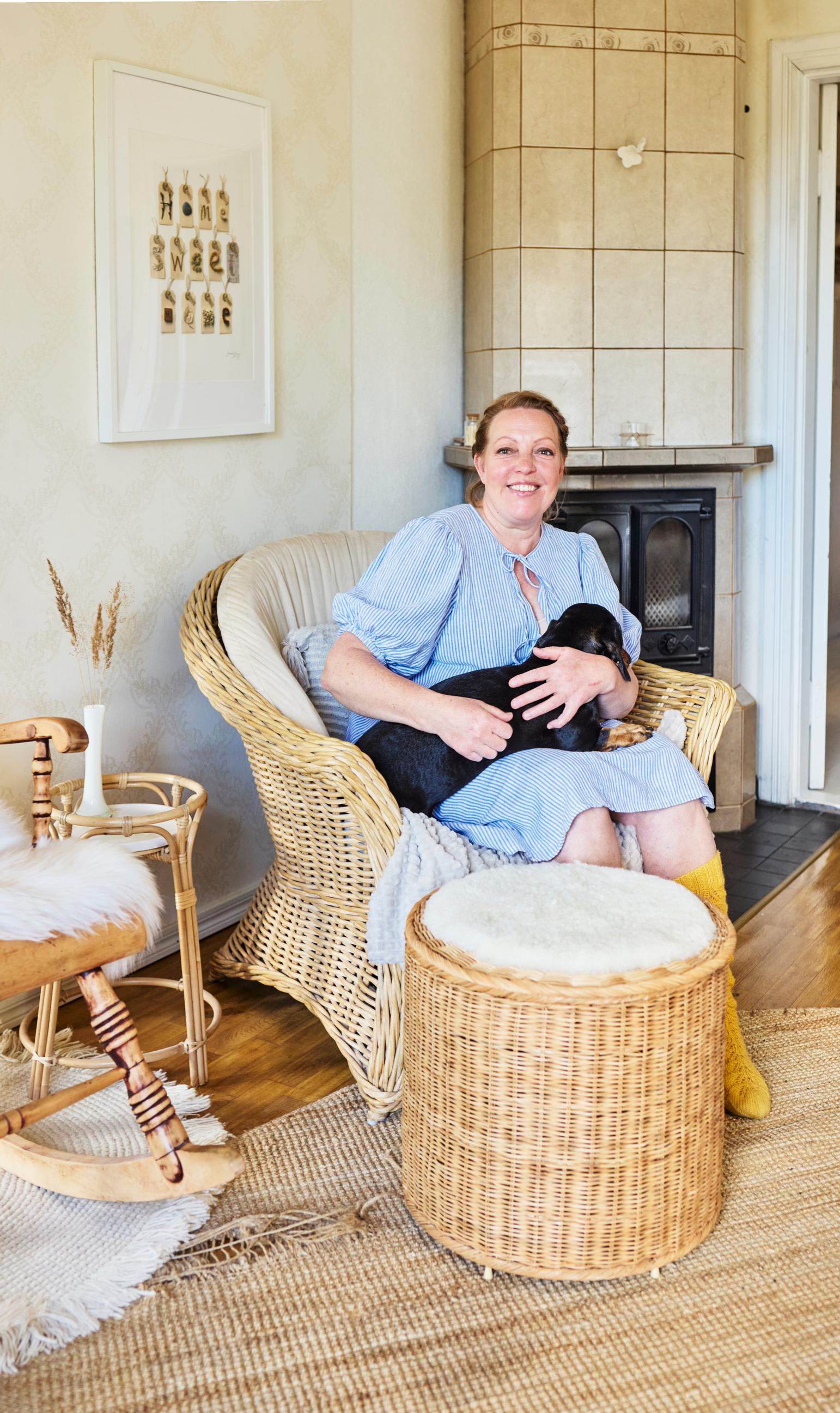 In the photo, a woman sits in a wicker chair with a dog in her lap.