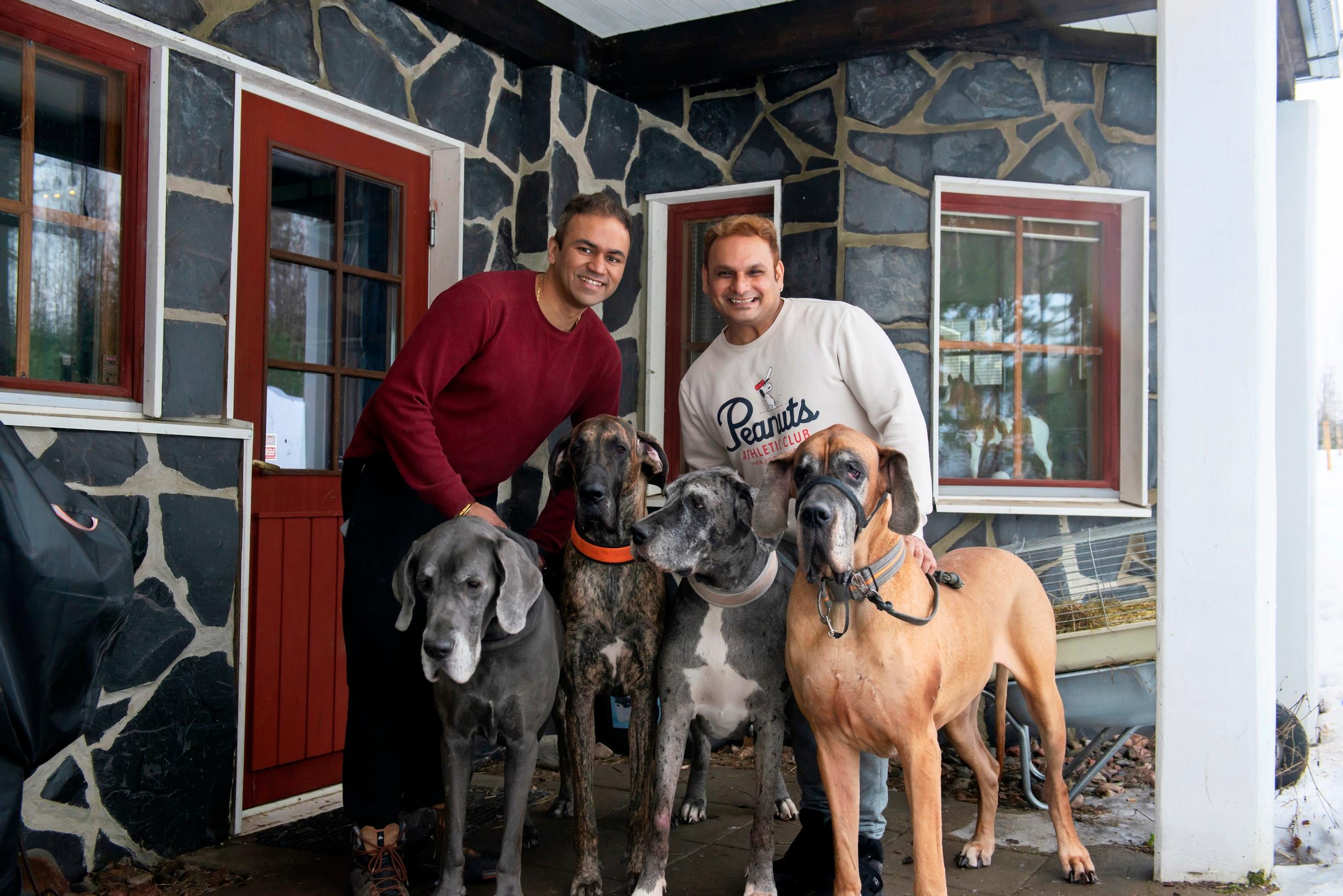two men and four dogs standing on the terrace in front of the house’s door
