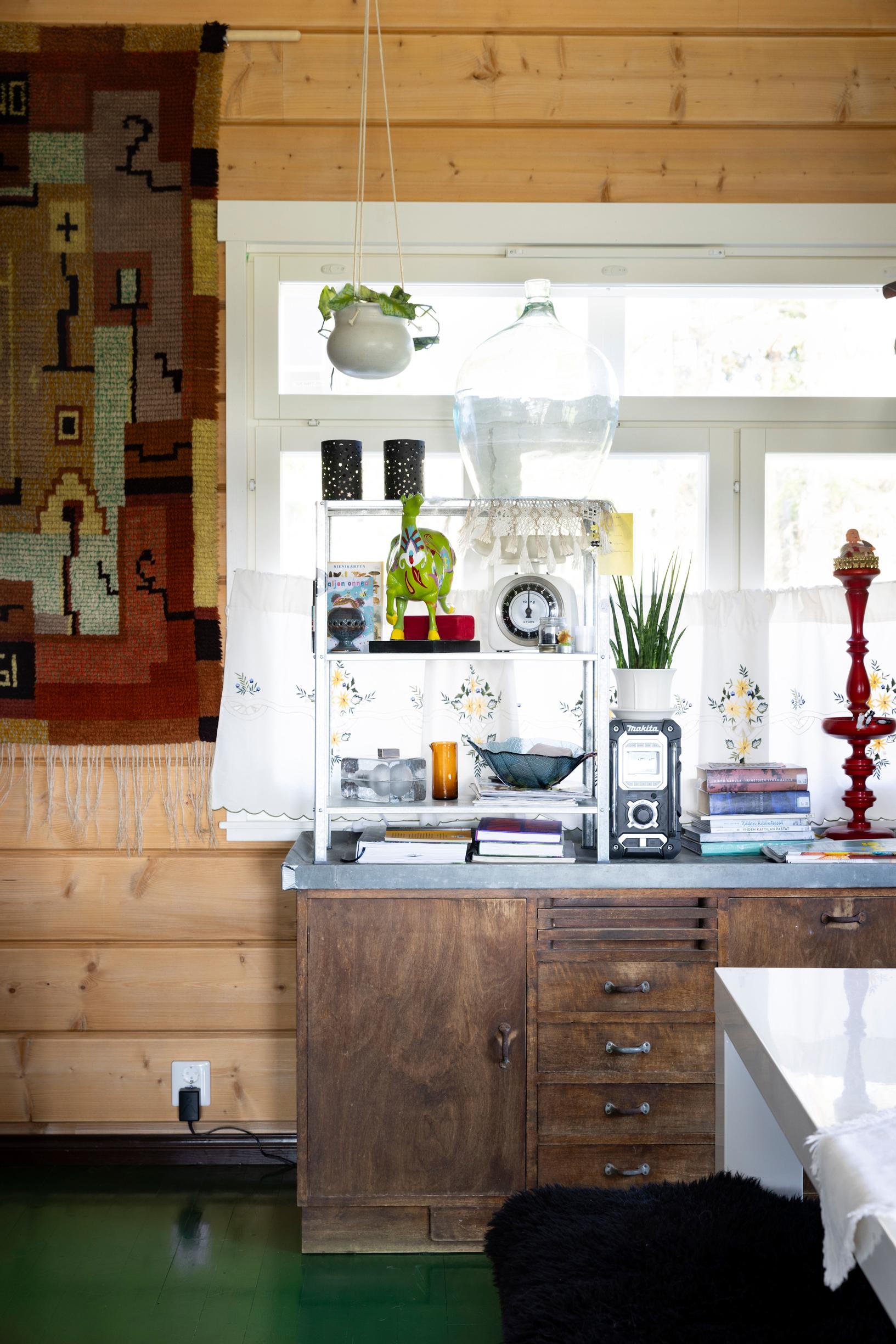 An old sideboard sits in front of the window, with a brown-toned tapestry on the wall.