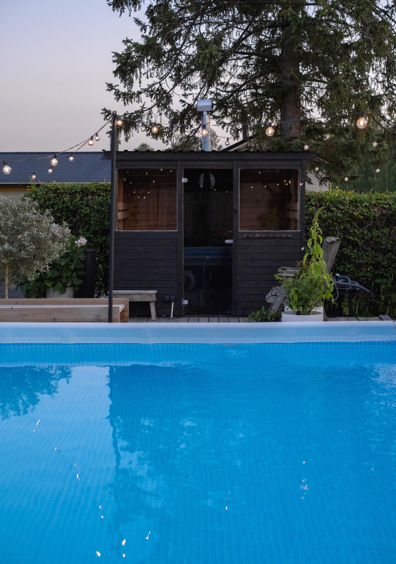 A dark, wood-paneled yard sauna next to the swimming pool