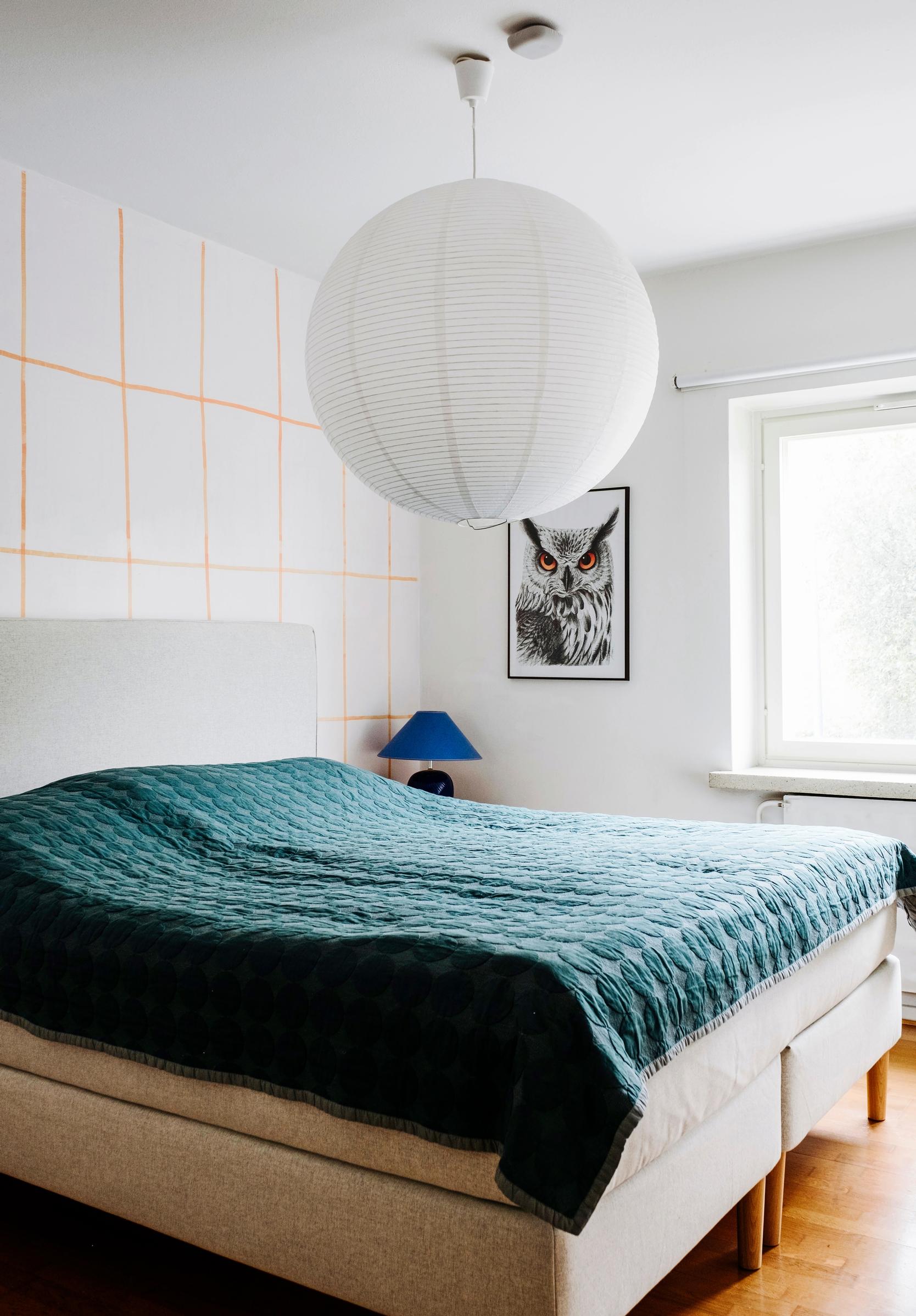 A double bed with a green bedspread and a yellow-checkered wall in the background