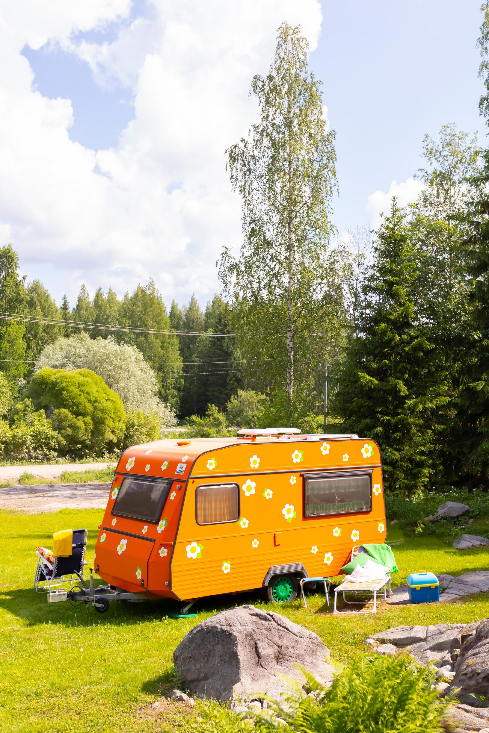 an orange, flower-decorated travel trailer on a lawn with forest in the background