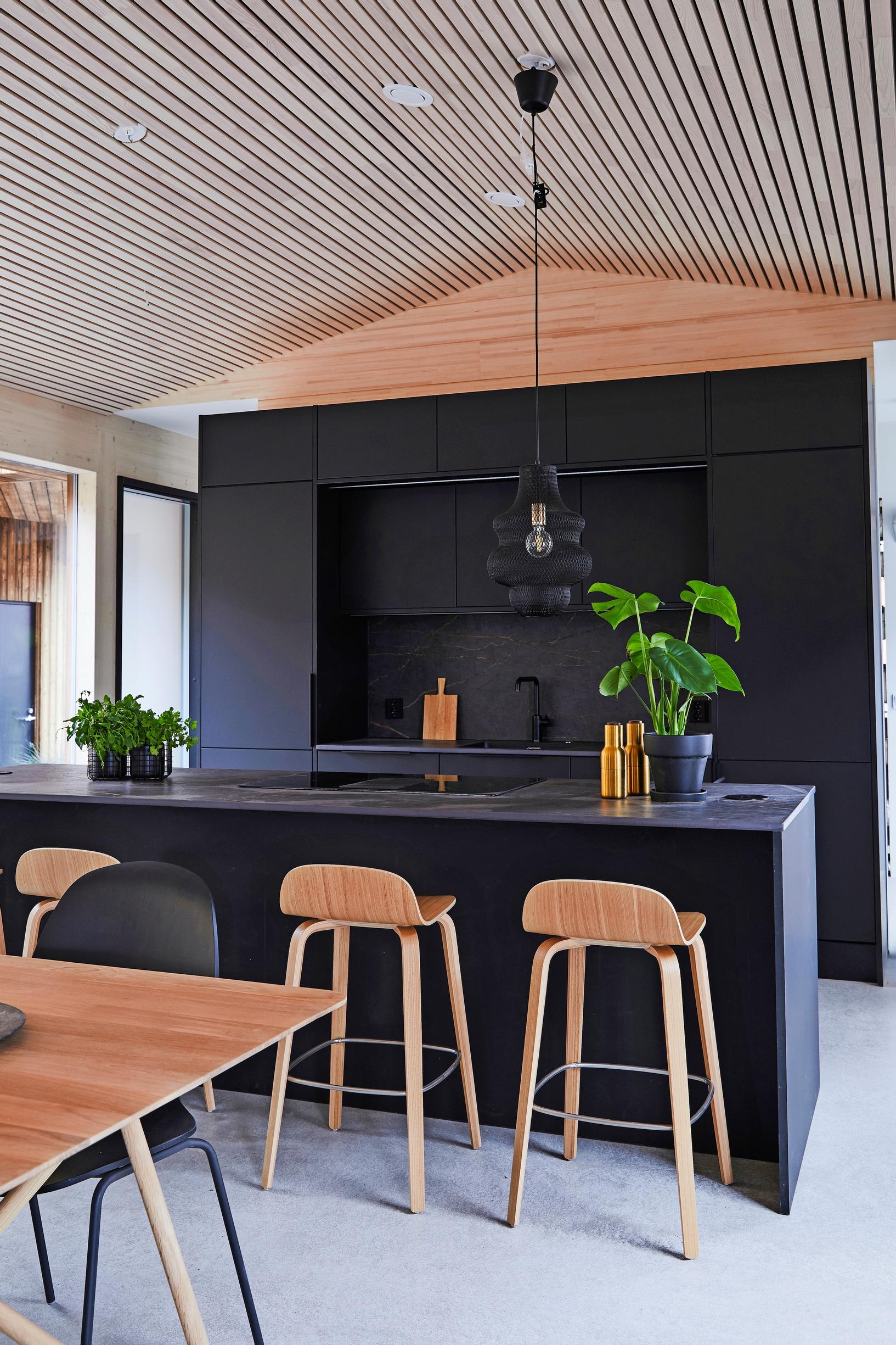 A slatted interior ceiling following the roof’s ridge shape. At the end, a black kitchen.