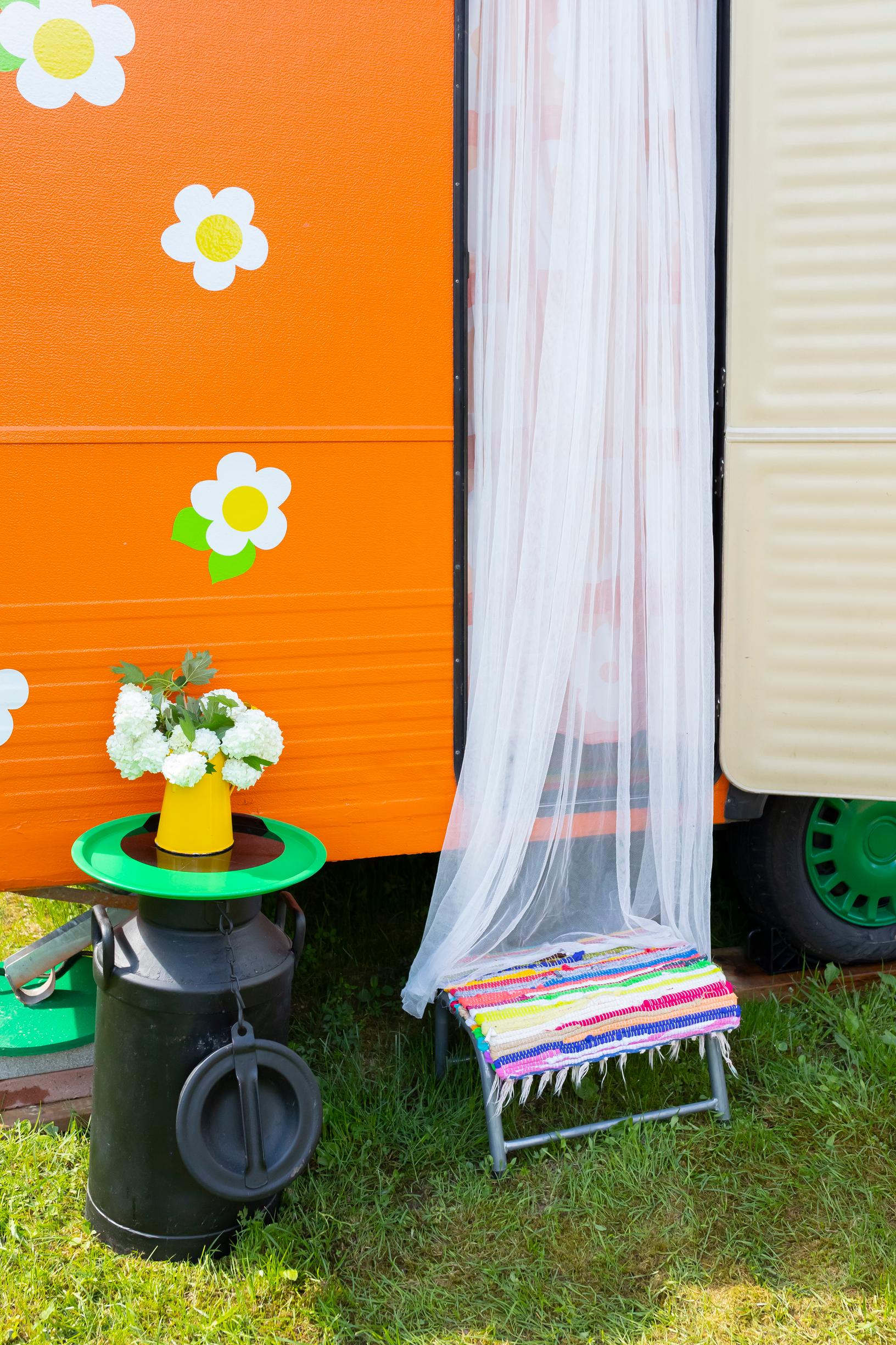 a mosquito net on the door of the colorful travel trailer and a milk can with a vase of flowers