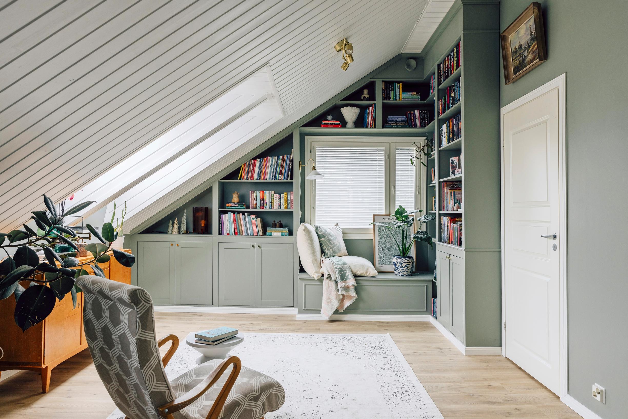 The green shelves are at the end of the room. On the left wall is an old dresser, and in the foreground there’s an armchair.