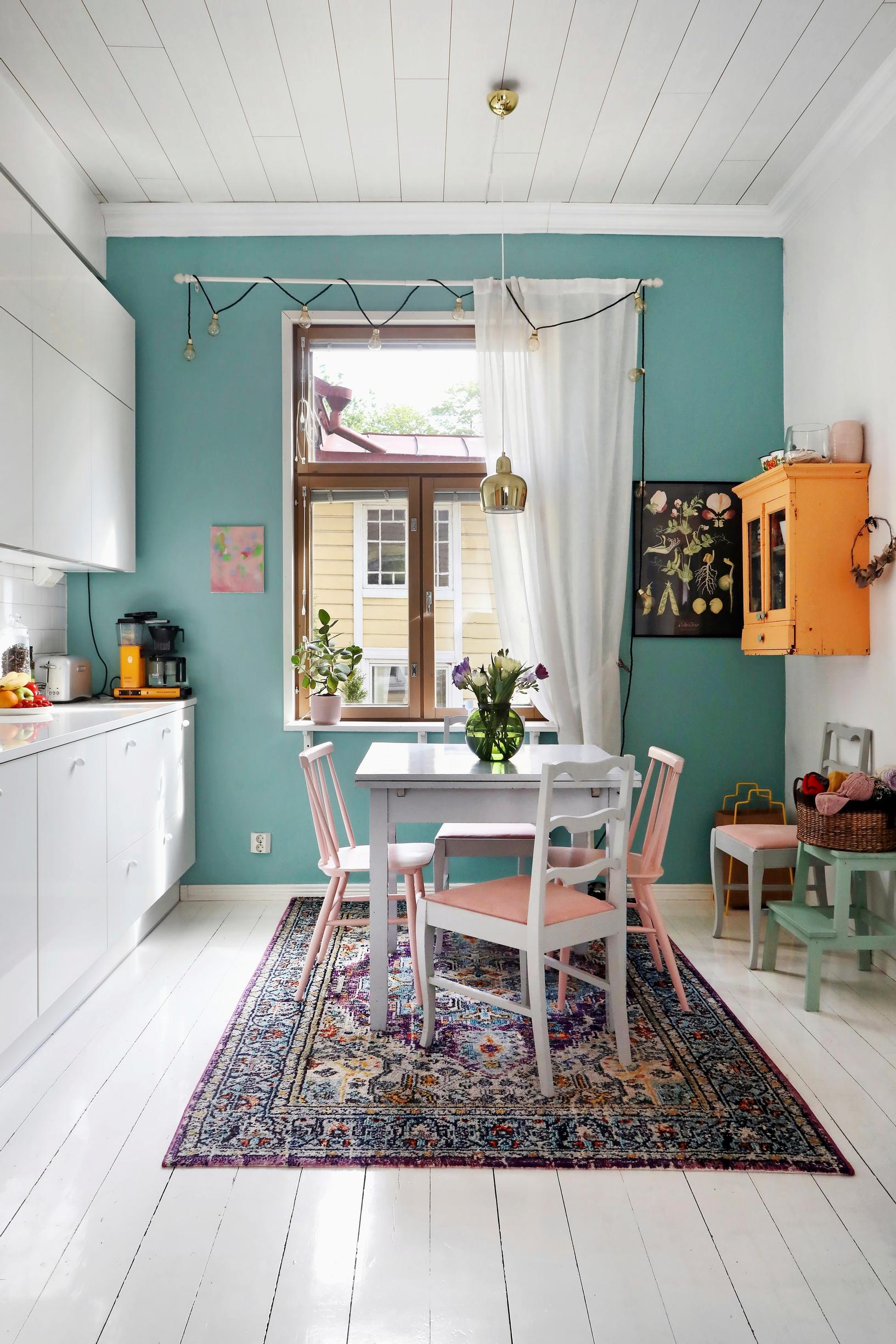 A photo of the kitchen in an old wooden home with a green accent wall and colorful furniture.