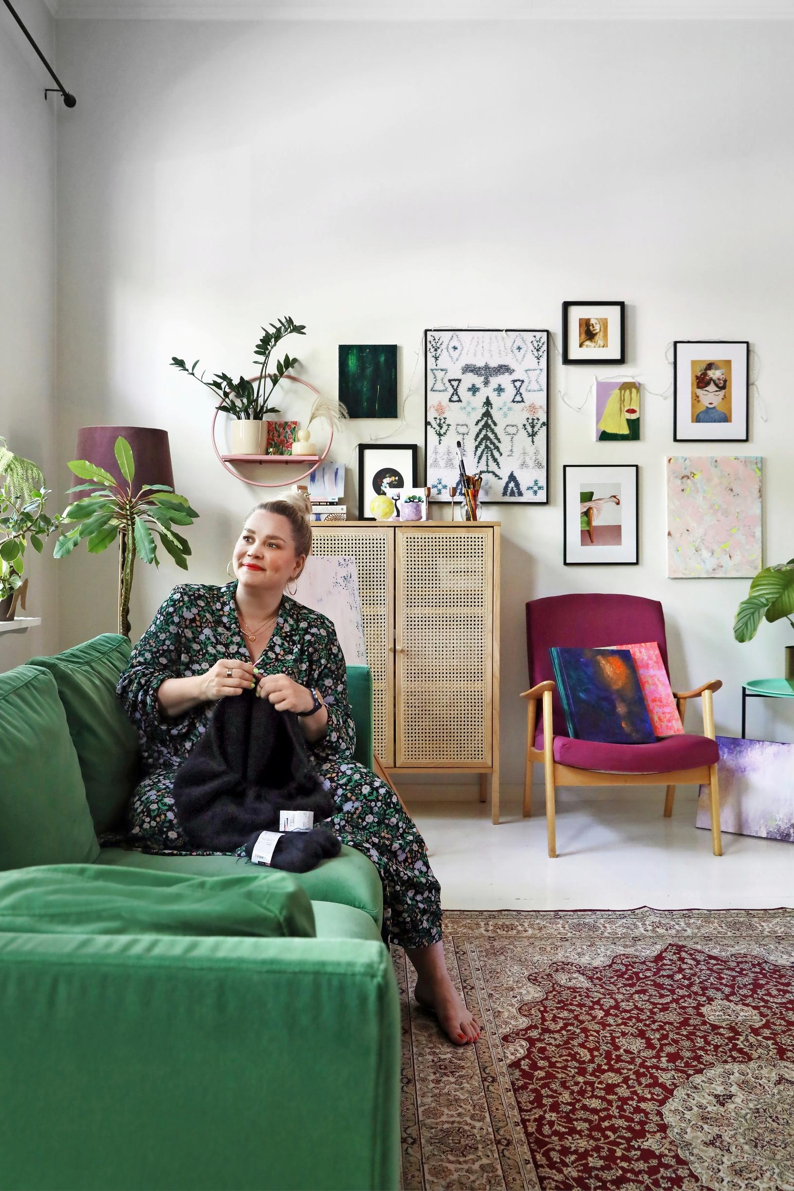 A photo of a woman knitting on a green sofa.