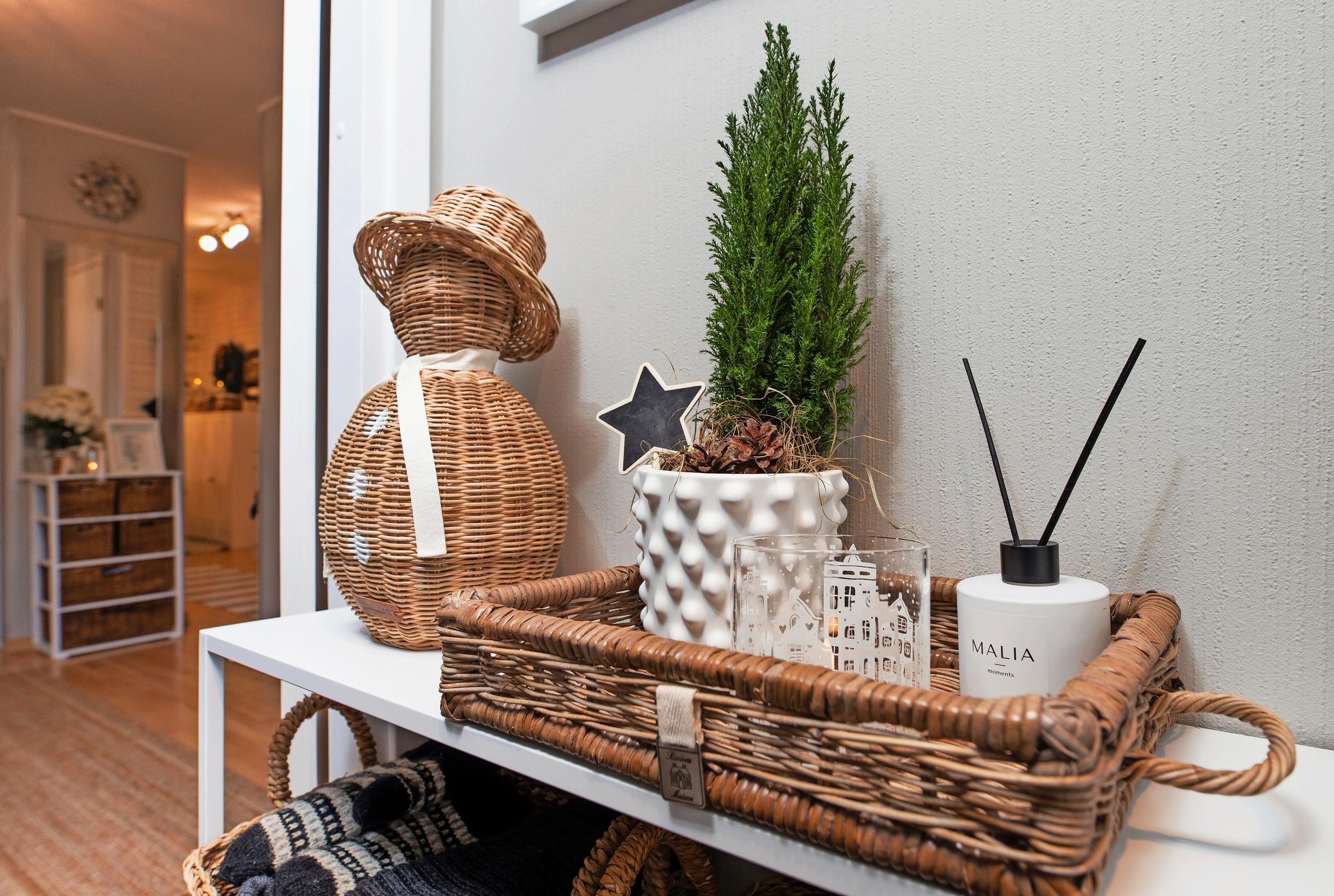On the table is a display with a rattan snowman and a rattan basket holding a green plant and a room diffuser