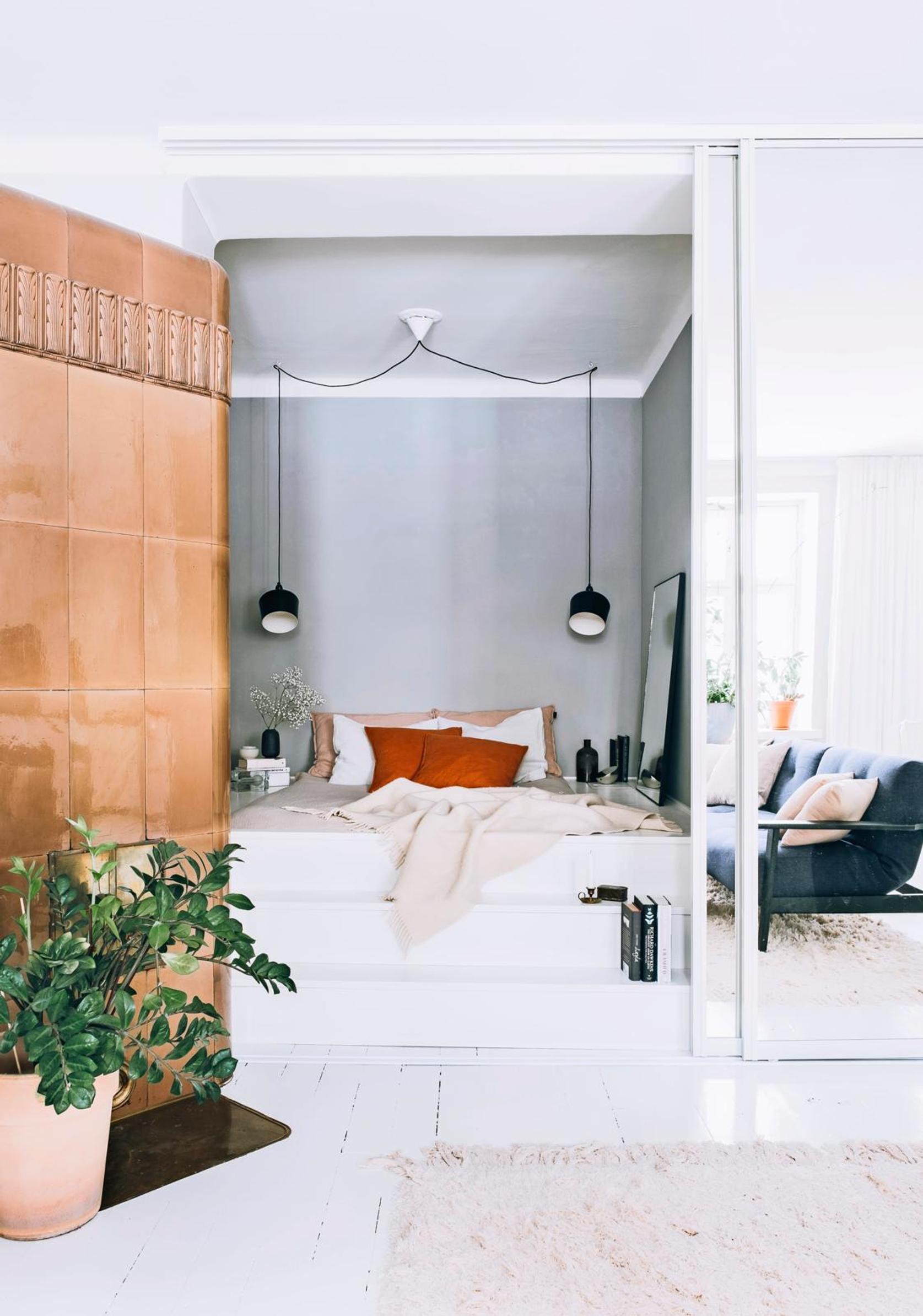 Three steps lead up to the bed. The back wall is bluish-gray, and black pendant lights serve as nightlights in the alcove.