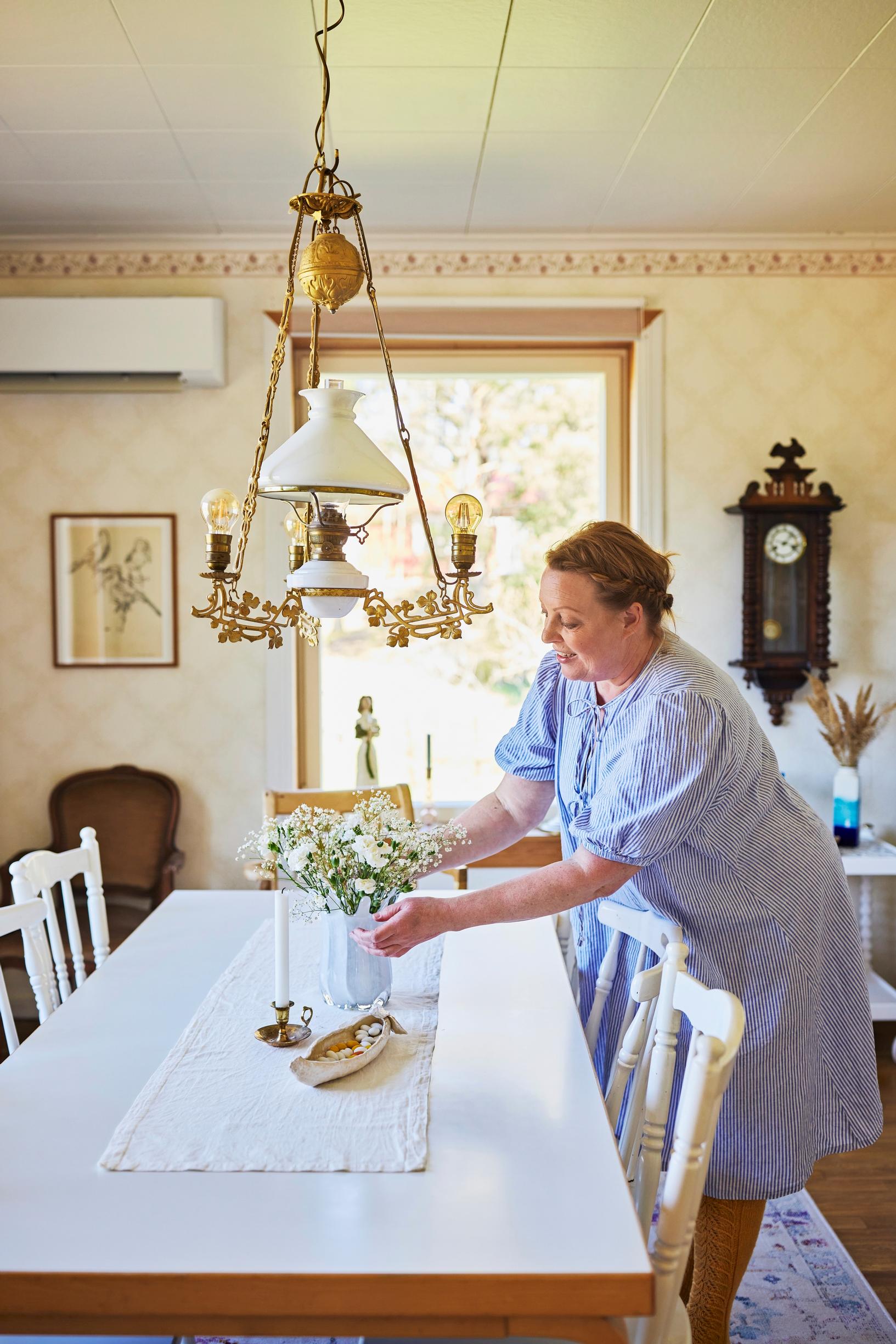 A photo of a woman arranging a vase of flowers on the table.