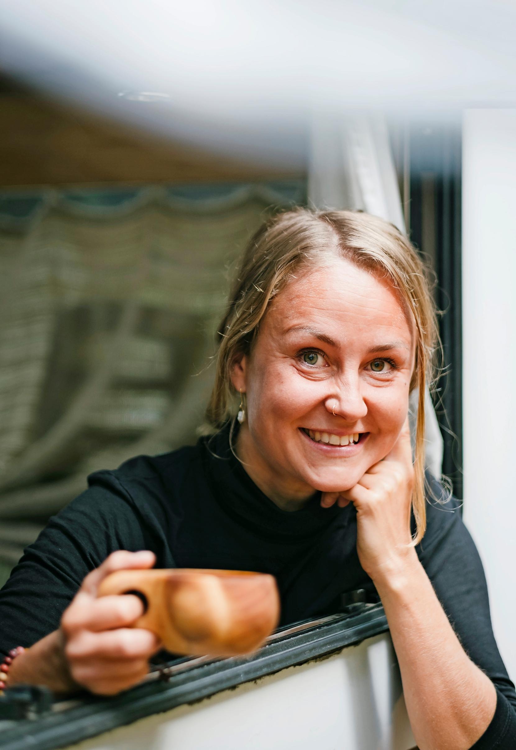 A woman looking out of a motorhome window, holding a kuksa cup