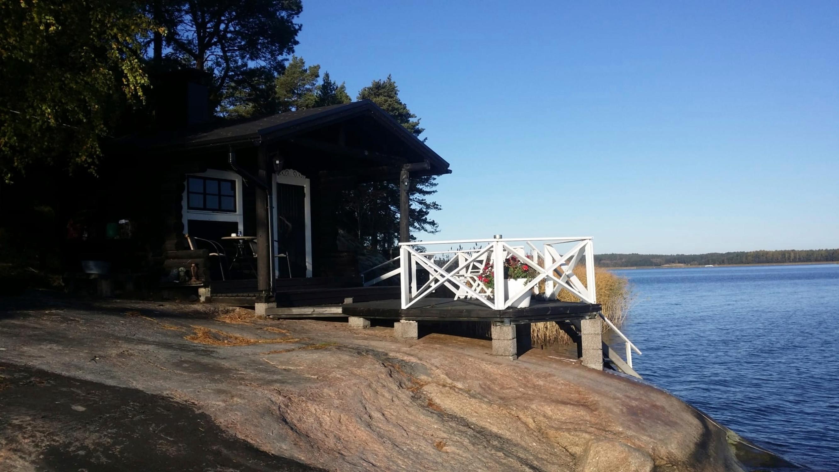 A dark shoreline sauna on the rocky coast by the sea, with a white terrace railing