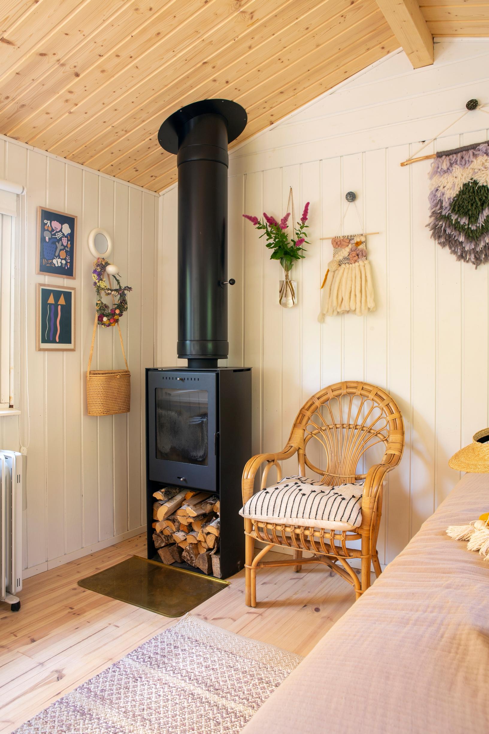 A corner of the main room with a black stove and wicker chair