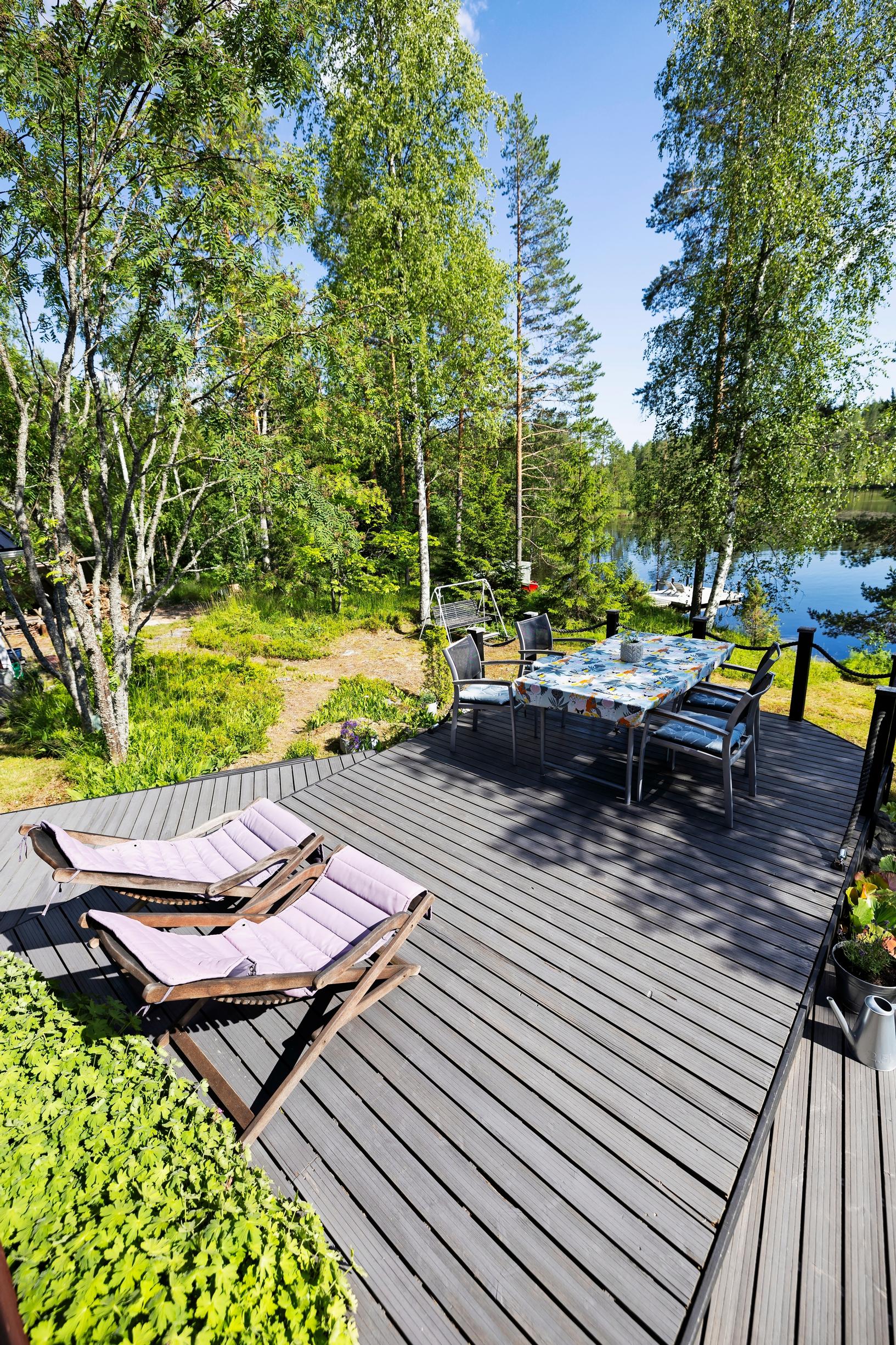 lounge chairs and a dining set on the deck, with a lake in the background