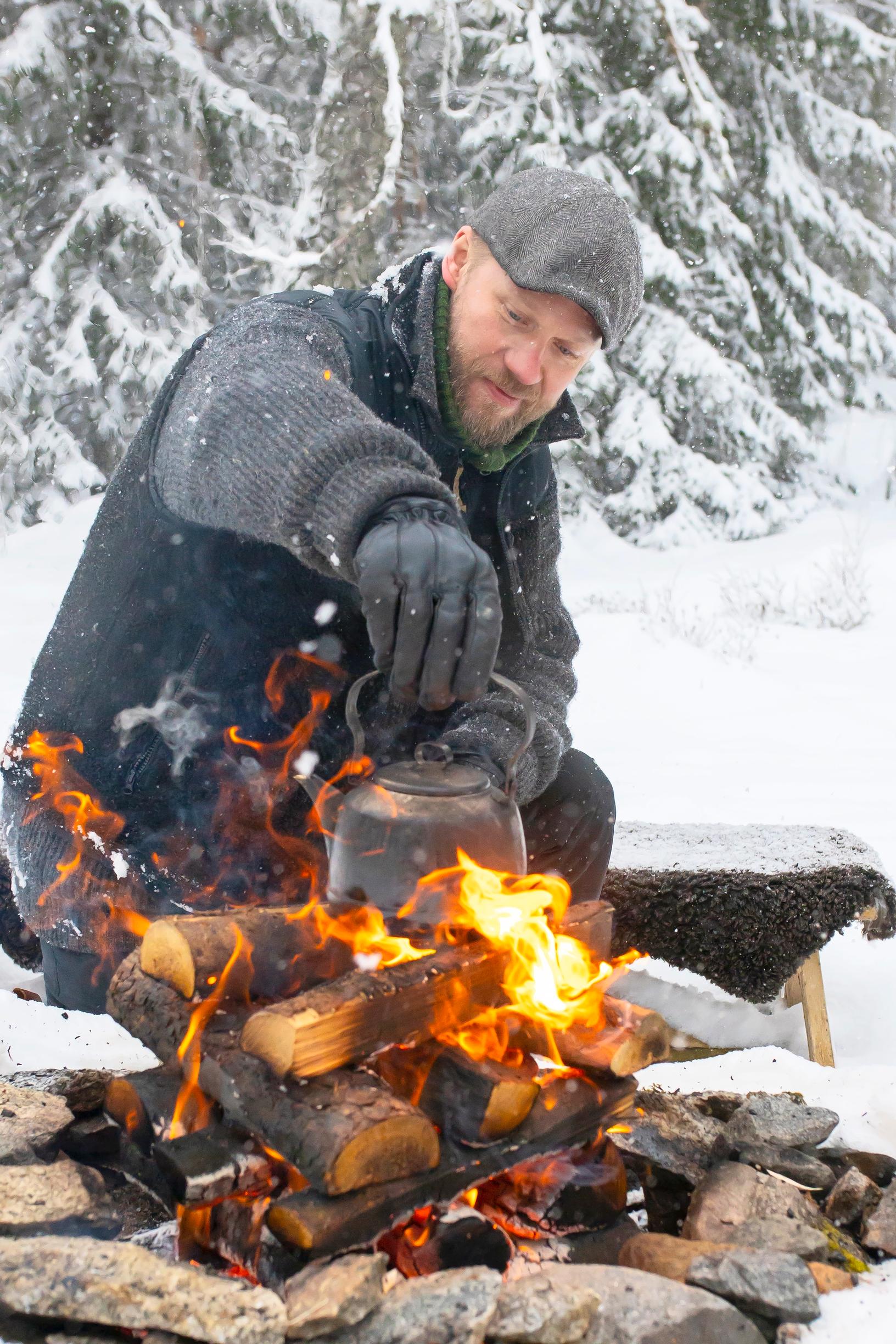 A man brewing coffee over an open fire in winter.