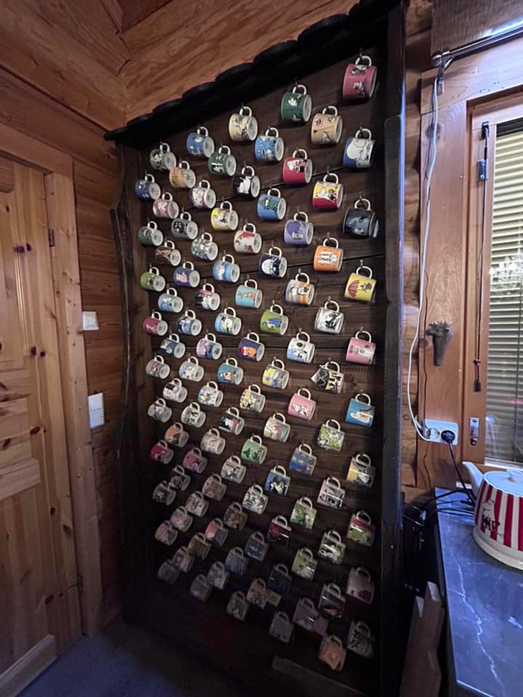 A wooden wall filled with Moomin mugs hanging on hooks