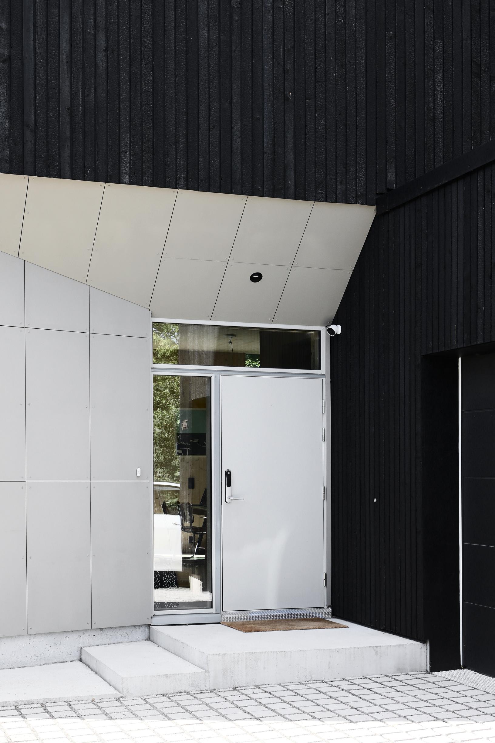 The exterior of the CLT house clad in black wood paneling. The entrance is highlighted with concrete panels.