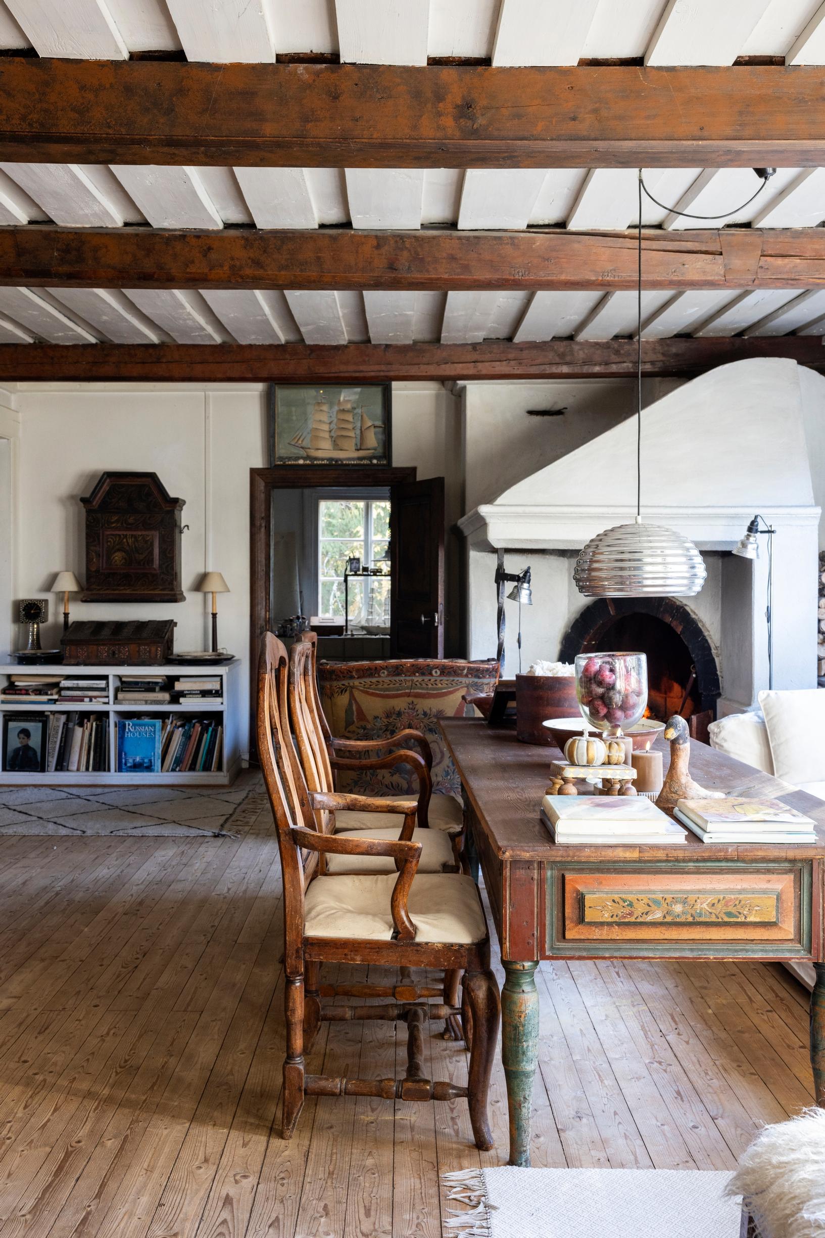Living room with two antique armchairs, a decorative painted table, and a large white open fireplace.