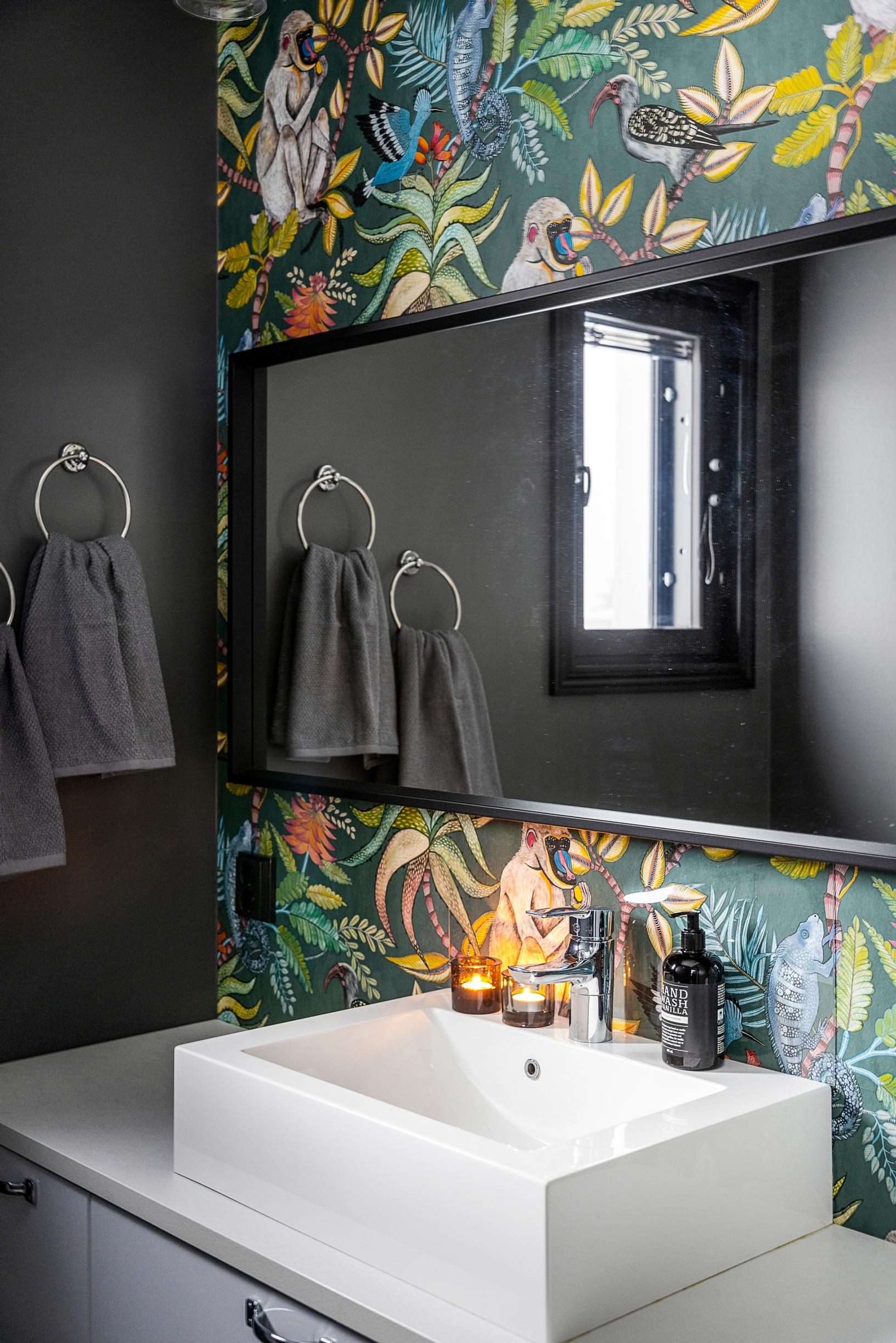 A dark bathroom with a rainforest-themed wallpaper on the wall.