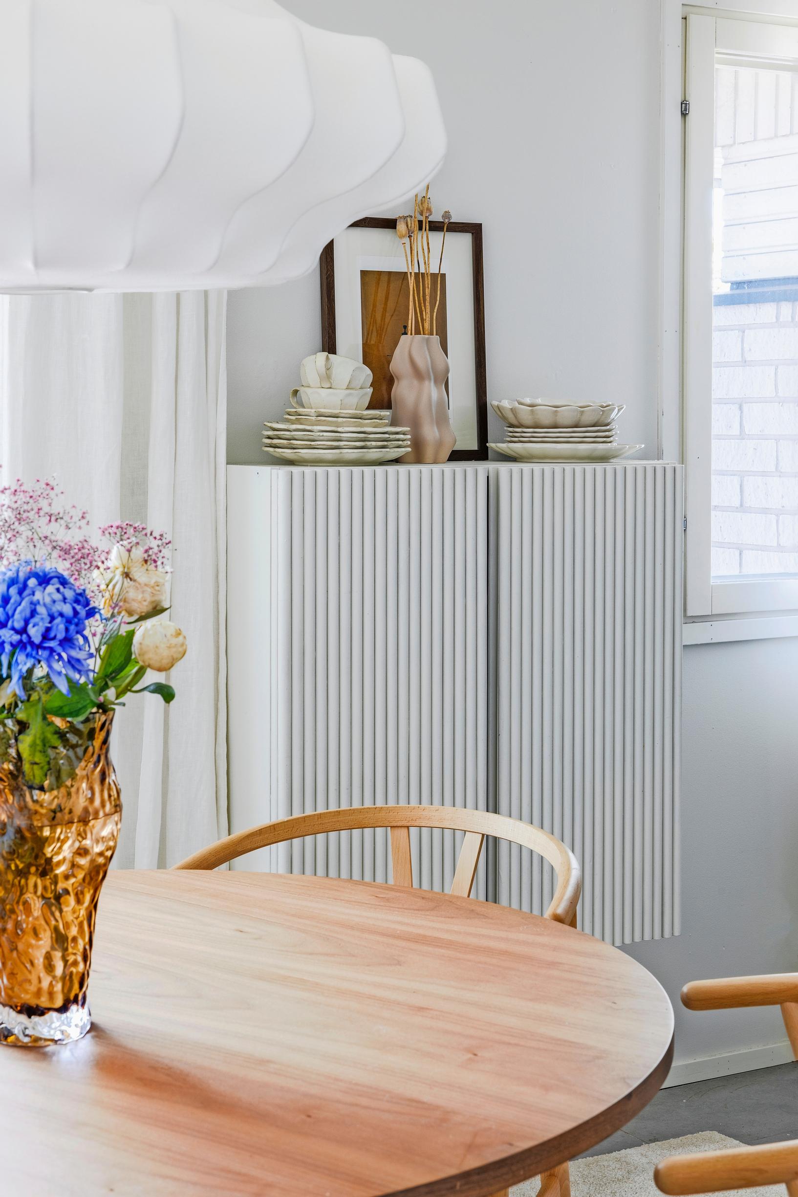 The doors are covered with slatting. The cabinet is painted white and mounted on the wall.