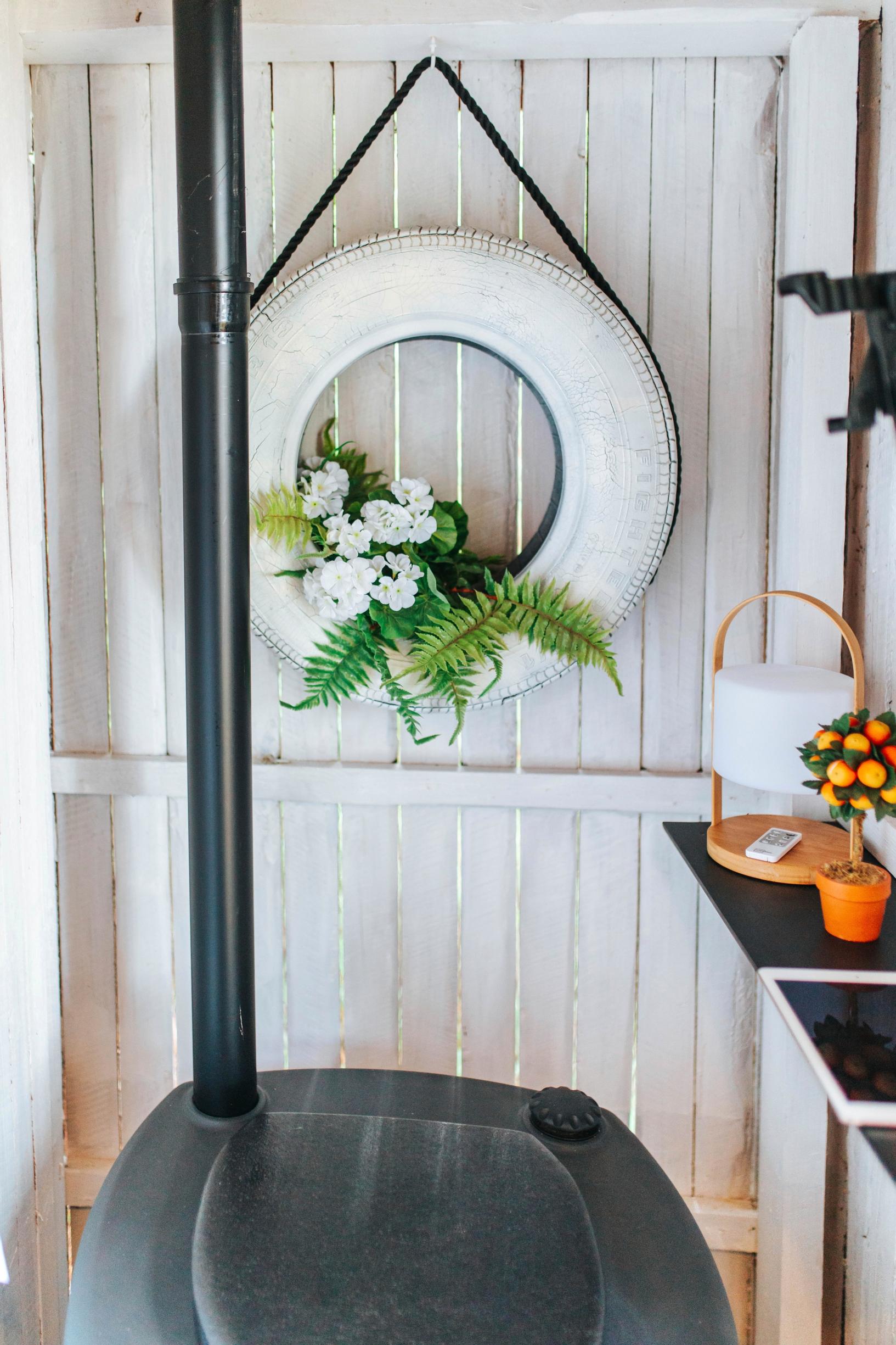A white-painted car tire embellished with faux flowers on the outhouse wall