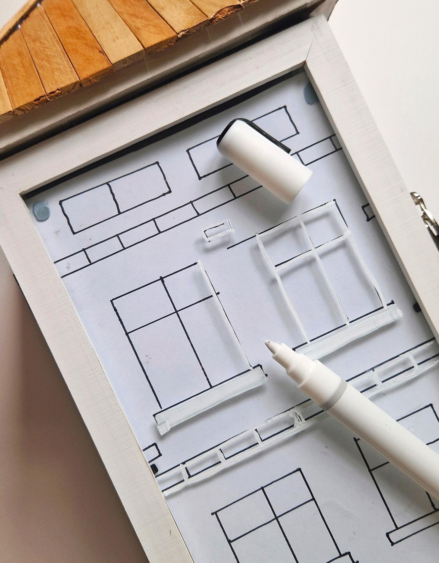 Use a white paint marker to draw the house’s details on the lantern.