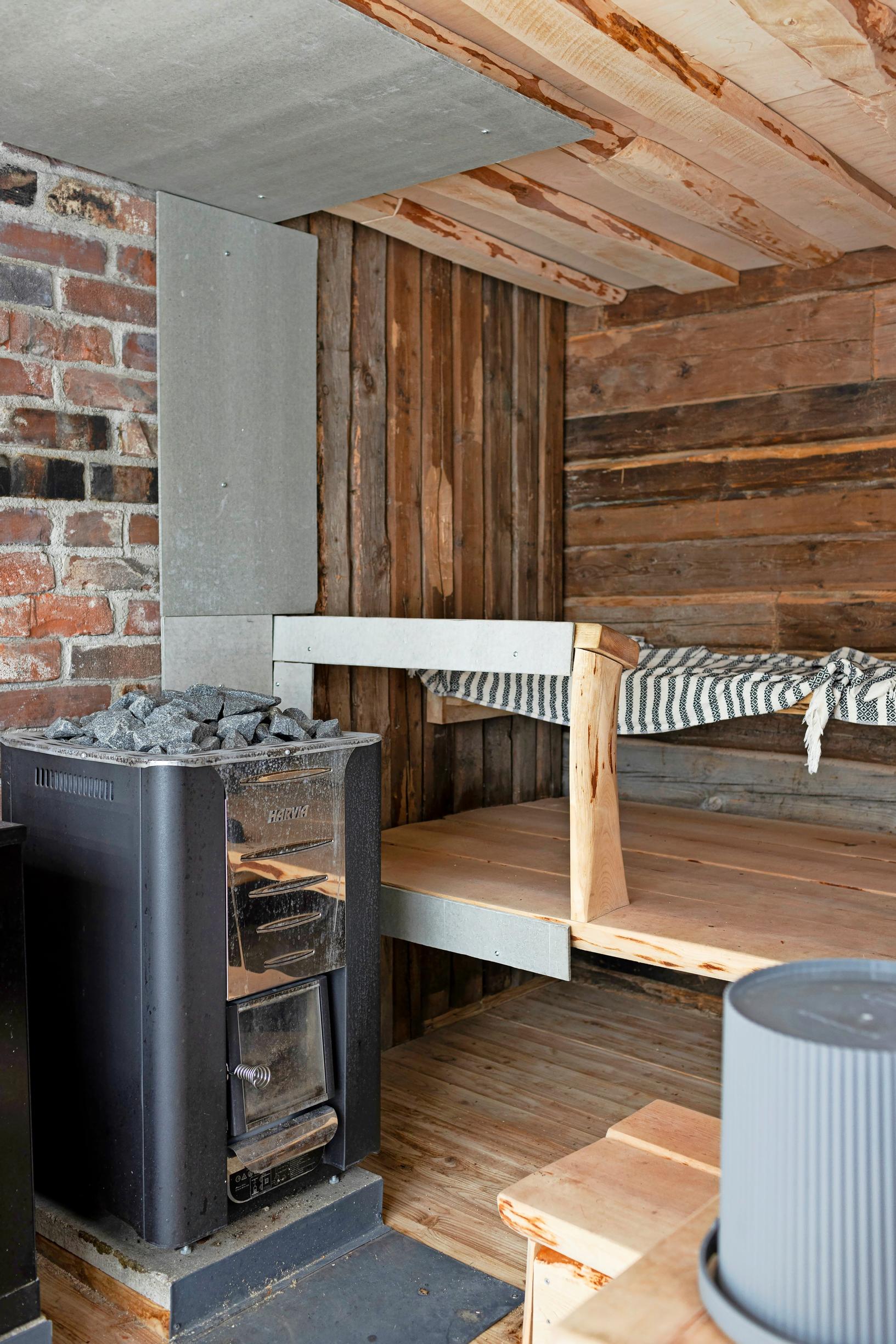 A sauna featuring wooden and brick walls, striped linens on the benches, and a stove.
