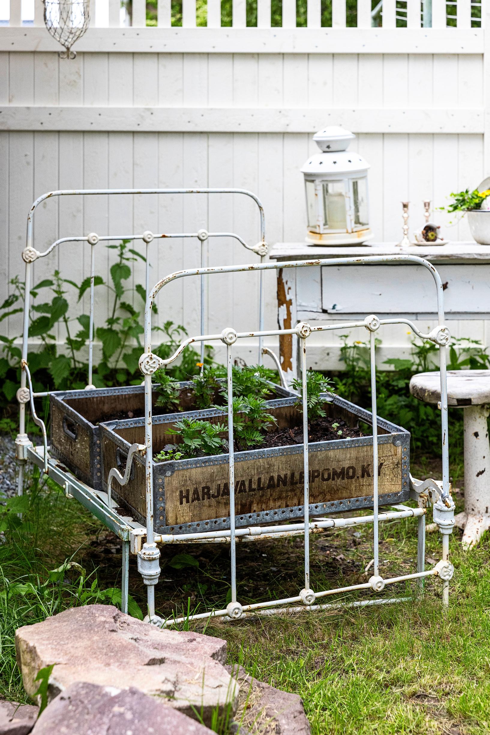 An iron bed frame and wooden crates repurposed as a place for summer flowers