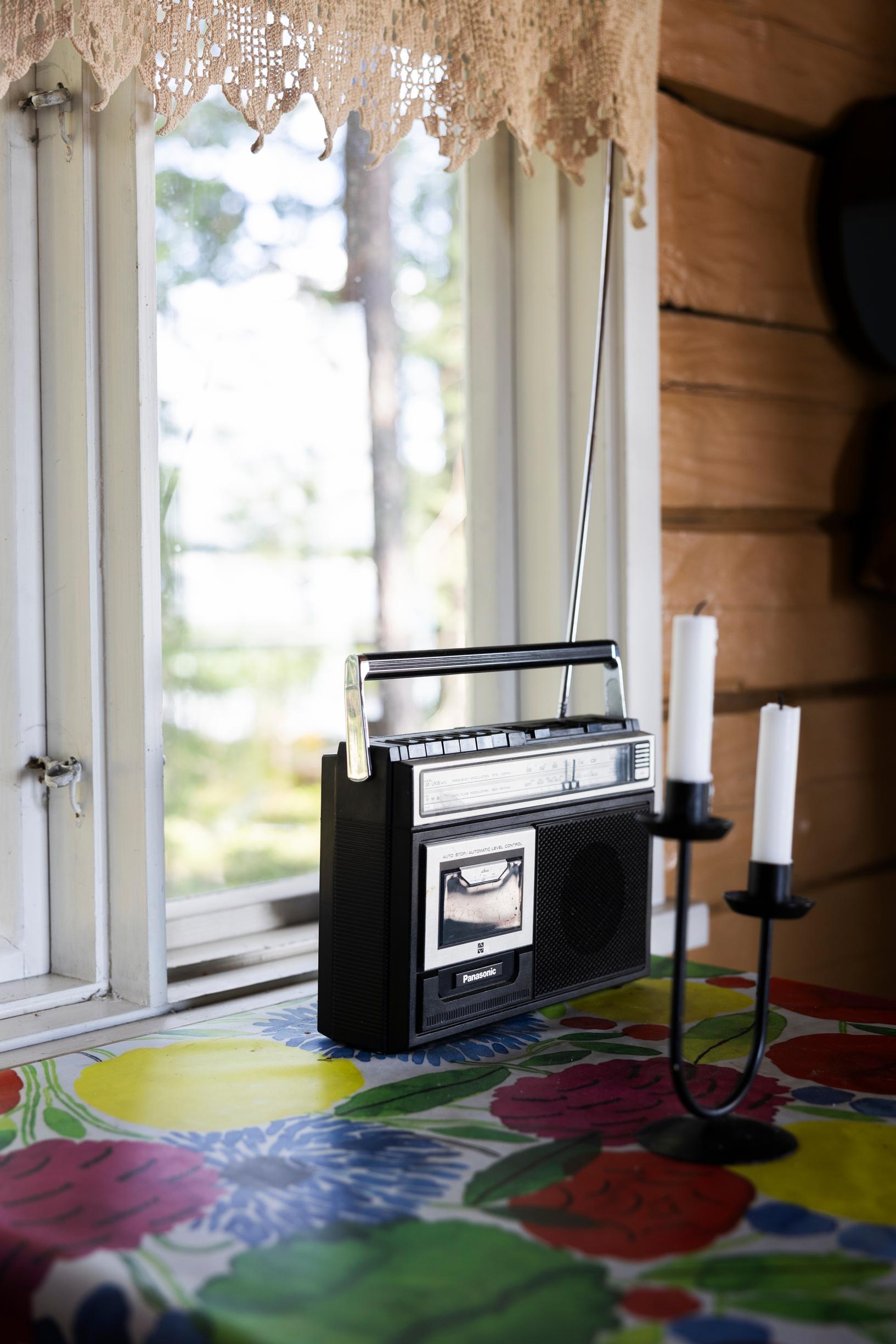 Boombox and two candlesticks on a table, colorful floral cloth, window