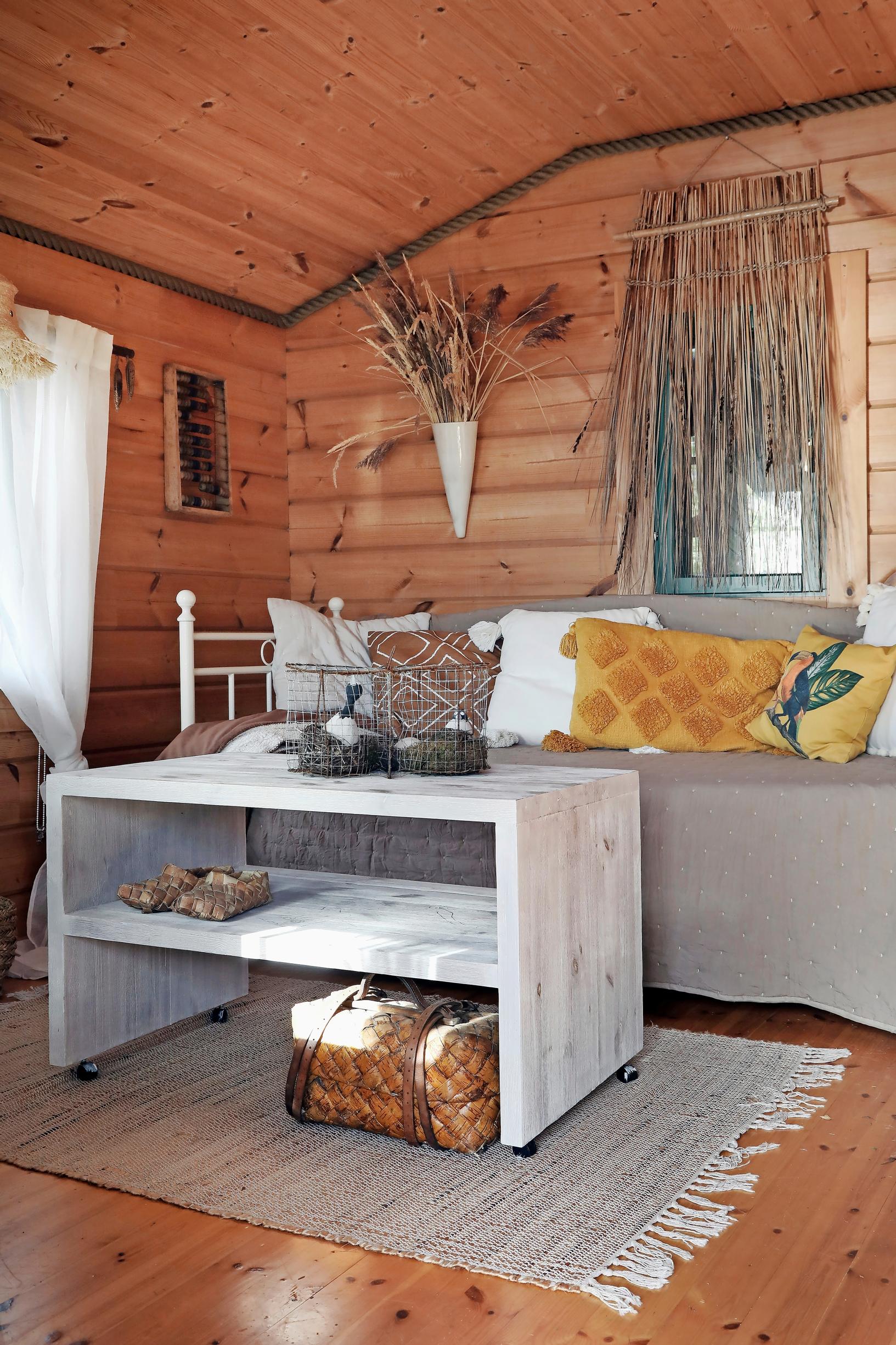 In the log building, sofa cushions on the bed, a light coffee table, and a reed curtain in the window.