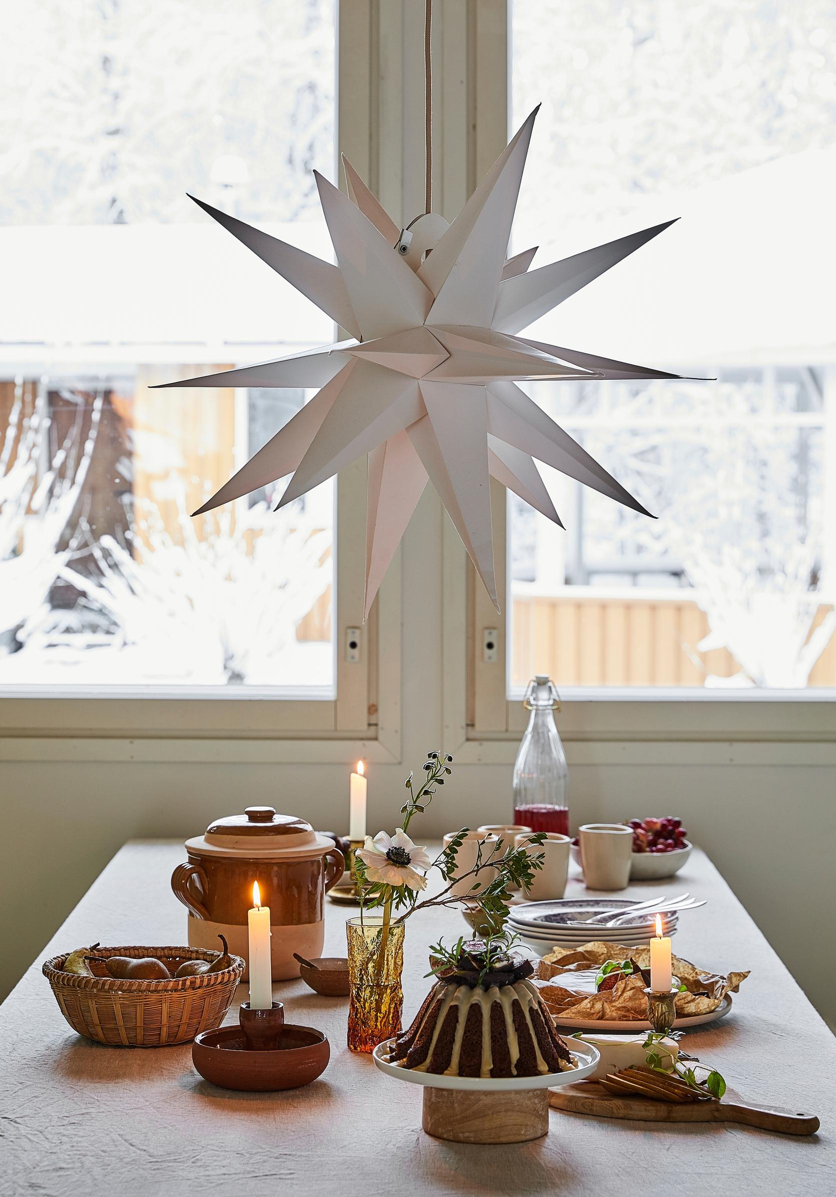 A white Christmas star hangs above a set table, with yellow buildings visible through the window