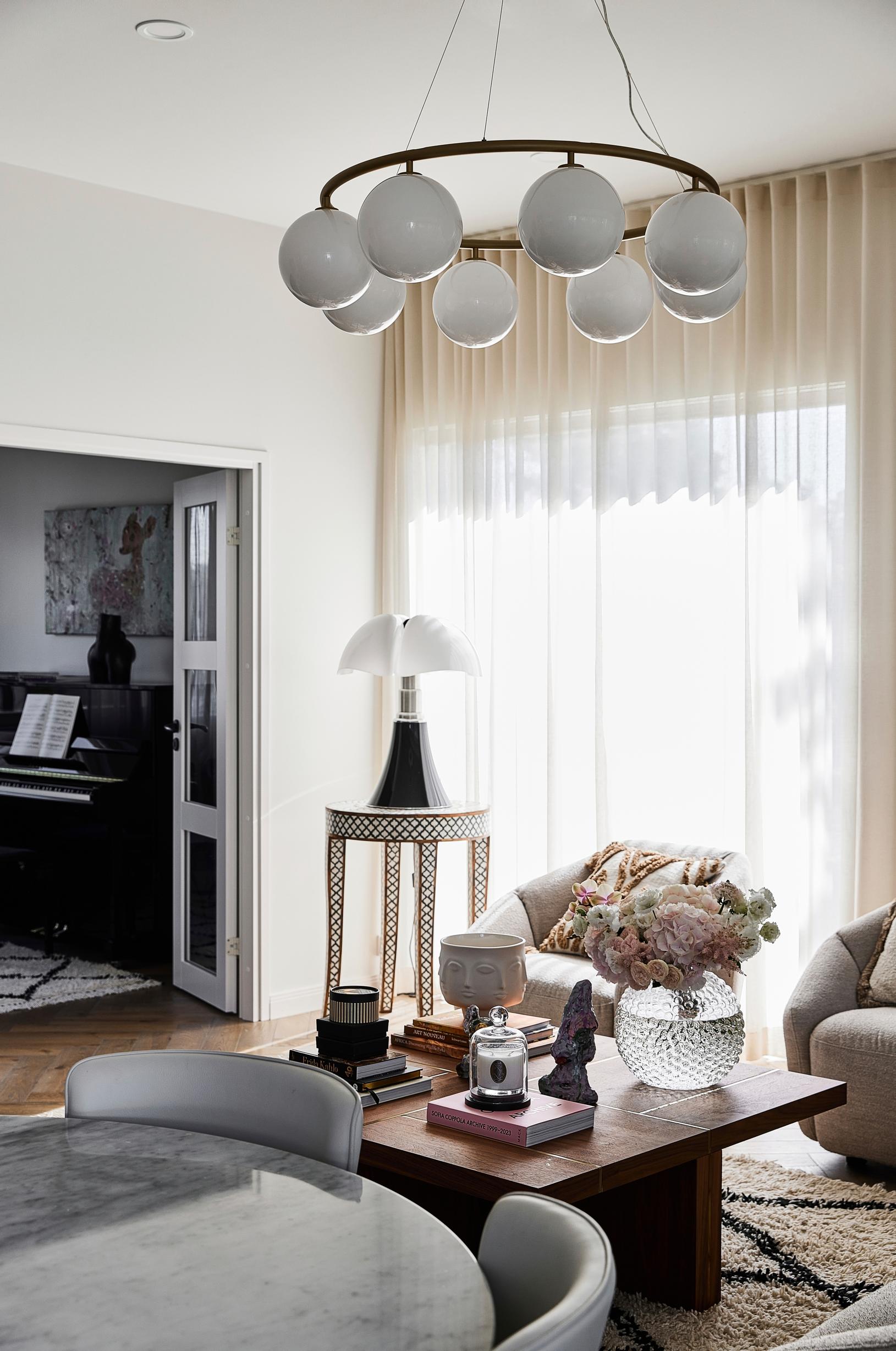 A coffee table with books and art objects. In front of the window is a small table with a table lamp.