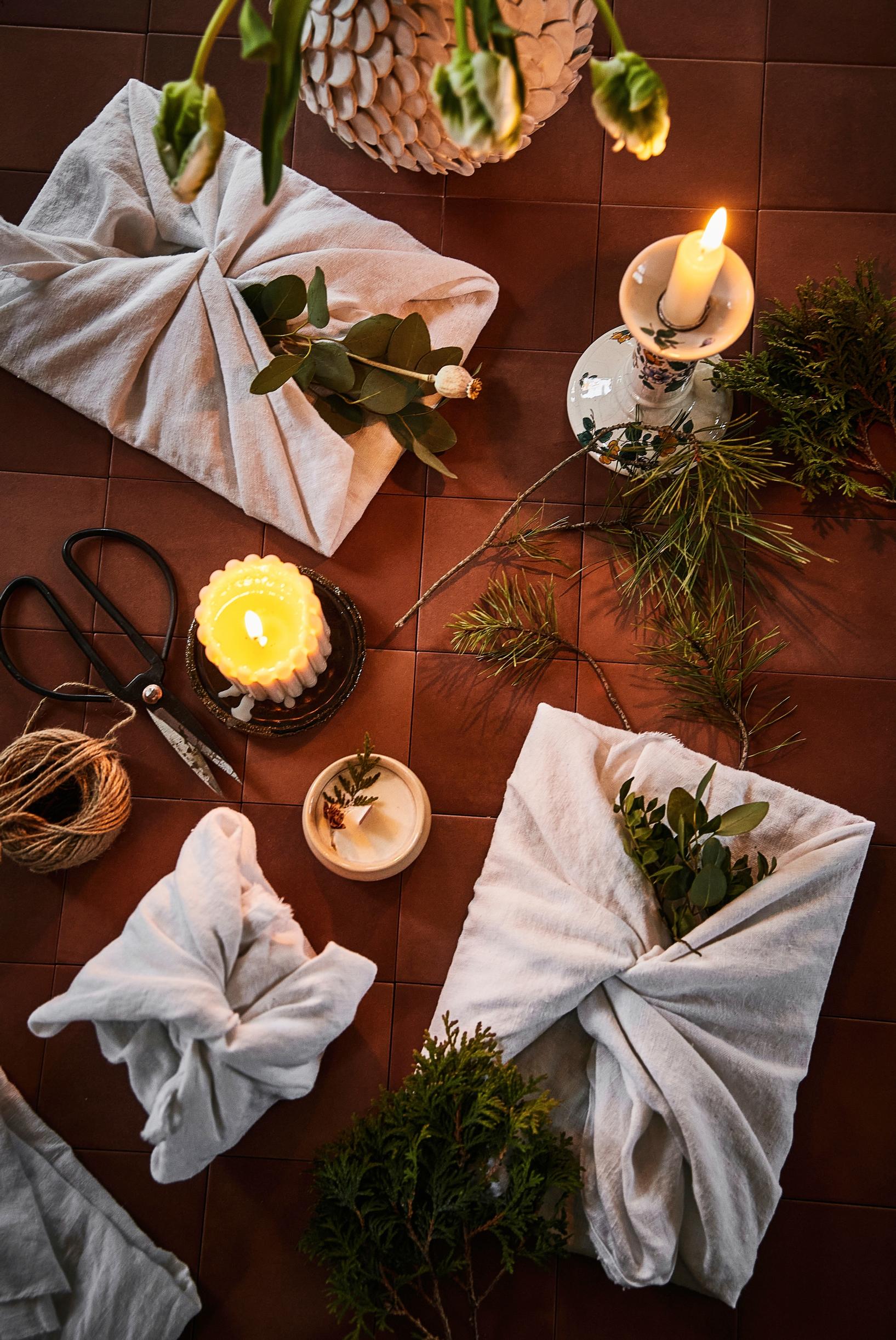 Packages wrapped in fabric, scissors, candles, and spruce branches