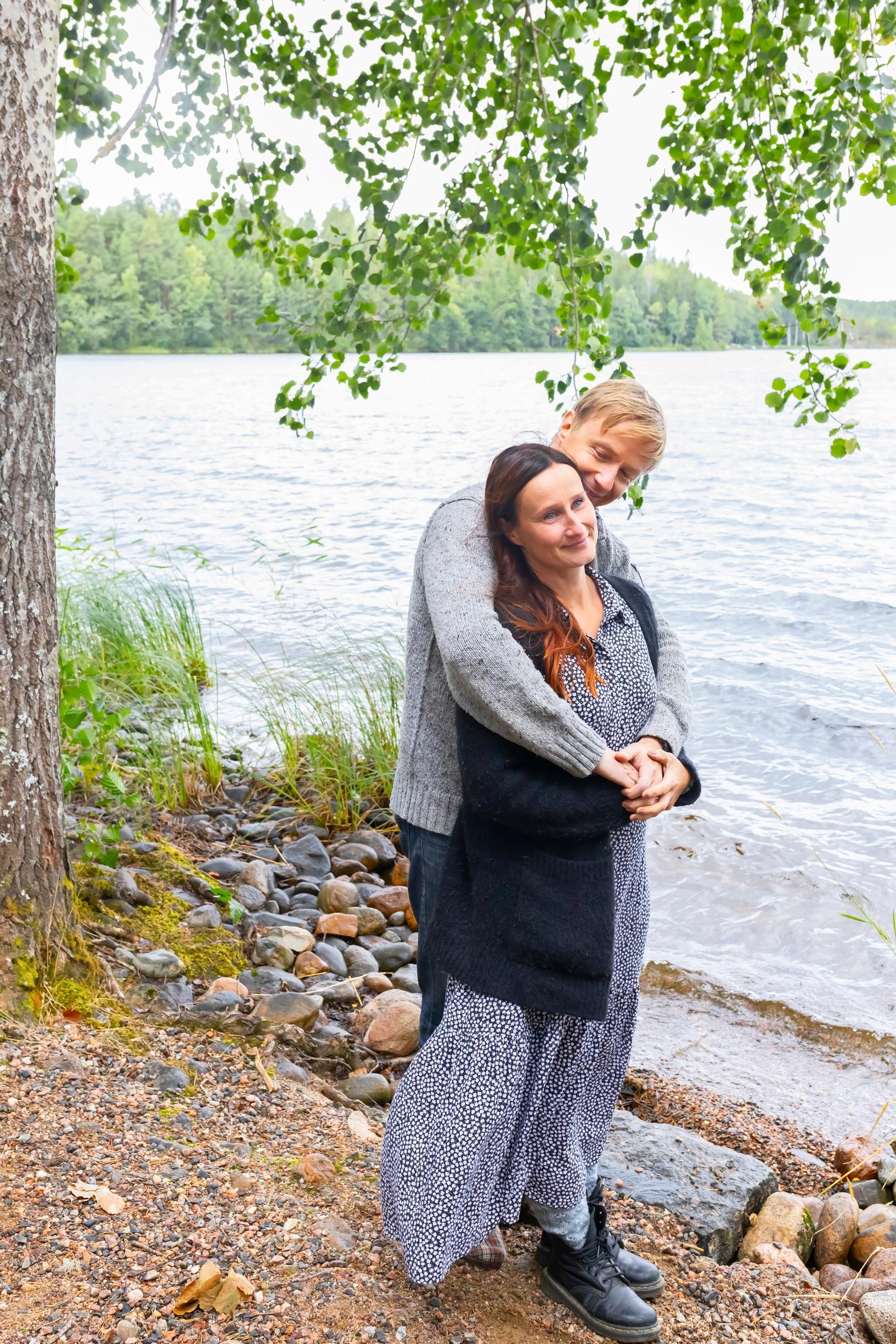 A couple standing by the lake, the man hugging the woman.