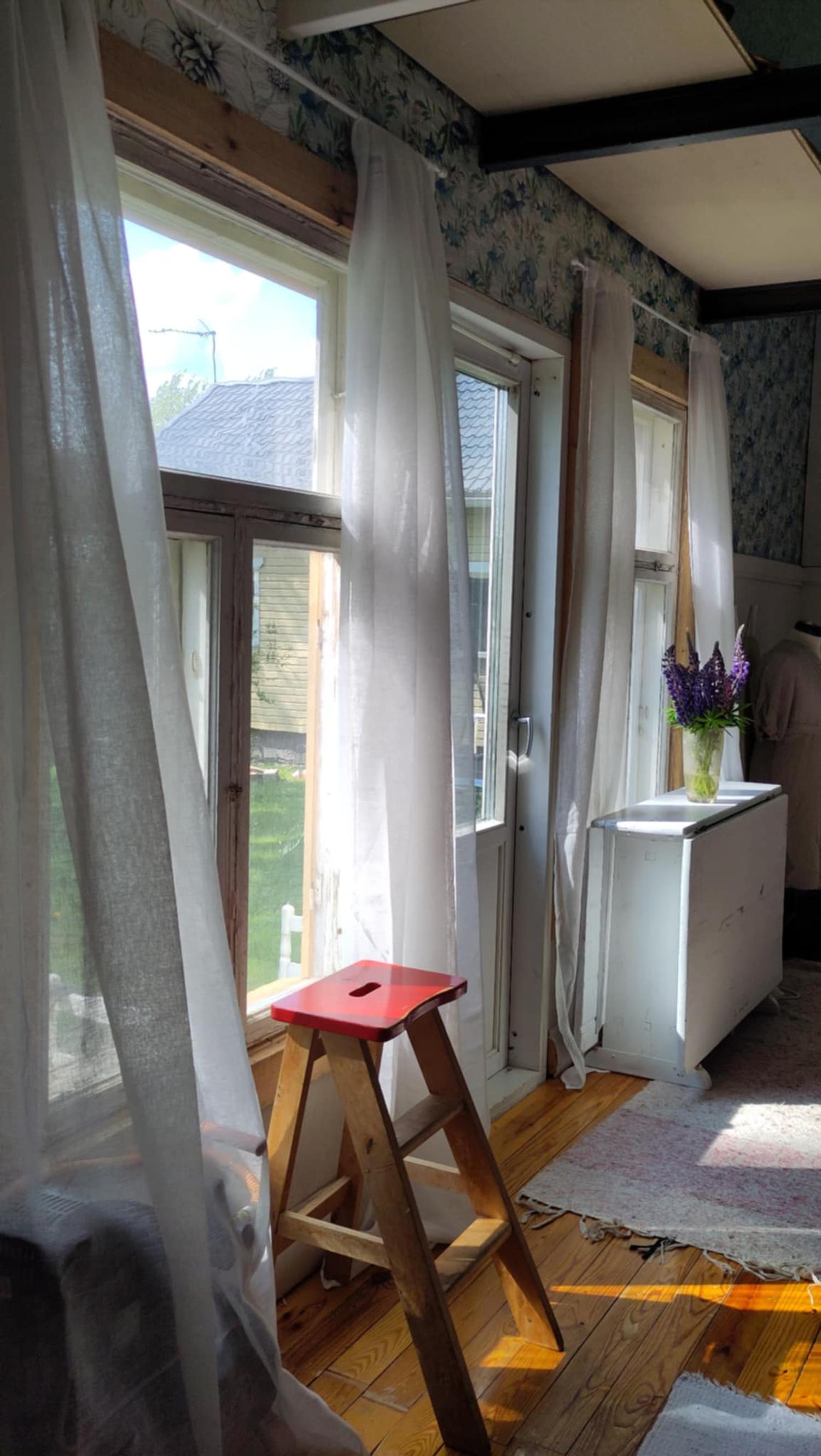 In front of the large windows are a small wooden stool, a white sideboard, and long white curtains.