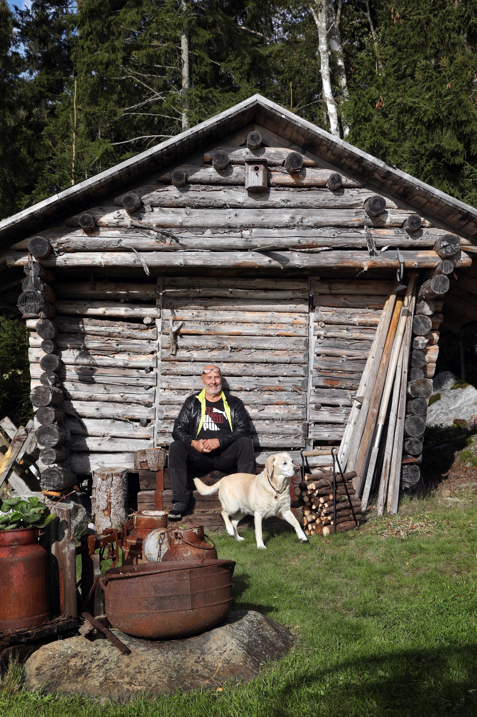 Markku Parkkari and the dog in front of an old log storehouse, with a rusted iron pot.